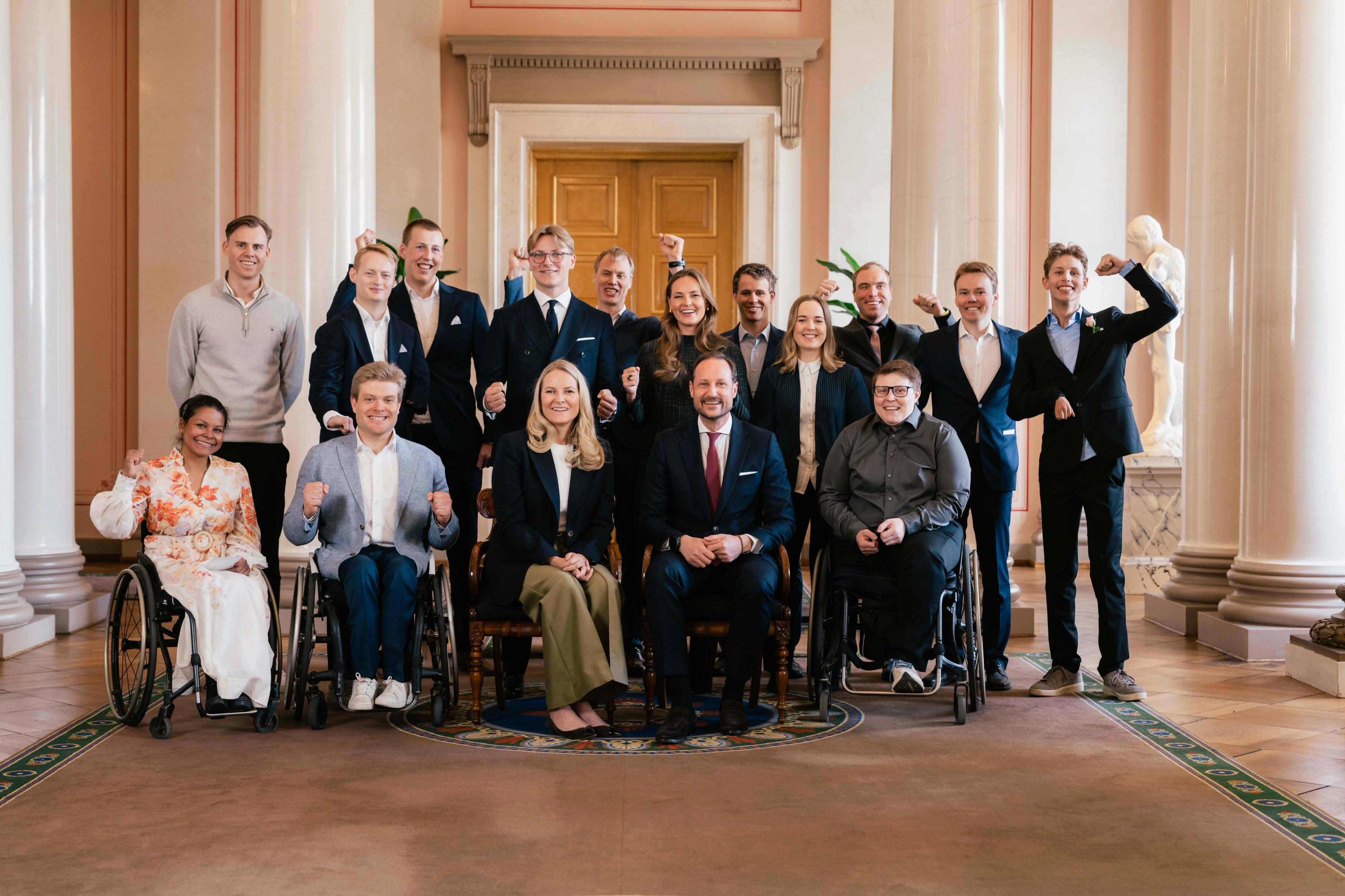 Kronprinsparet, Prinsesse Ingrid Alexandra og Prins Sverre Magnus omgitt av de norske deltakerne i Paralympics 2026. Kronprinsparet sitter på første rad sammen med utøvere i rullestol, mens Prinsessen og Prinsen står på andre rad sammen med de andre utøverne.