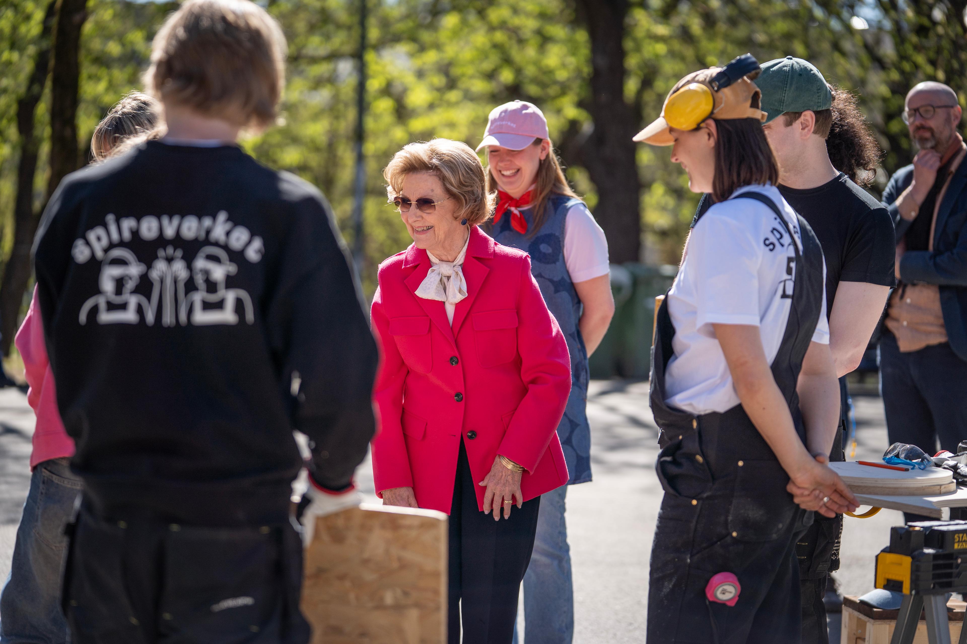 Dronning Sonja står i en ring med unge voksne i arbeidsantrekk for møbelsnekring.