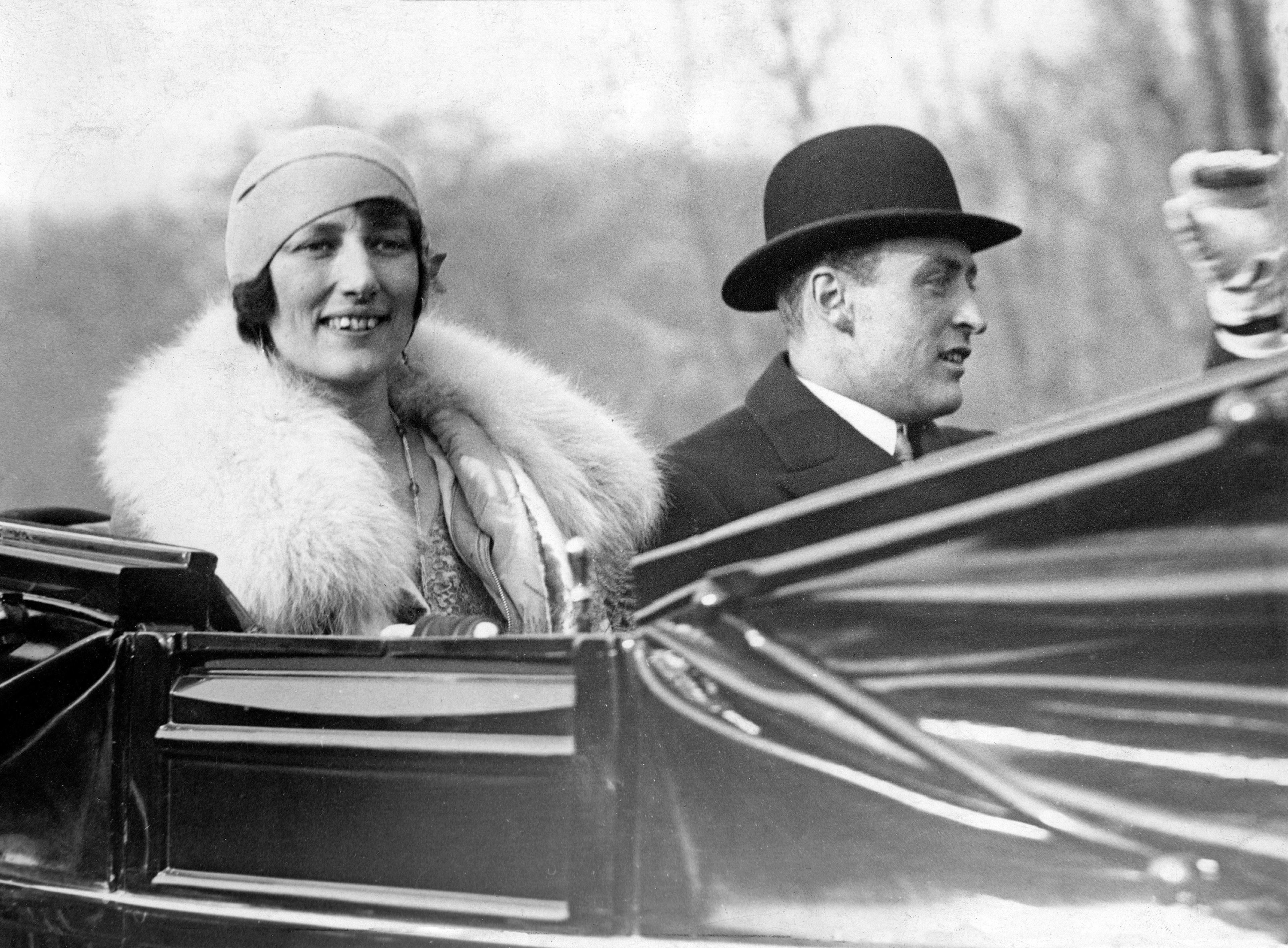 Kronprins Olav og Kronprinsesse Märtha smiler og vinker fra åpen bil.