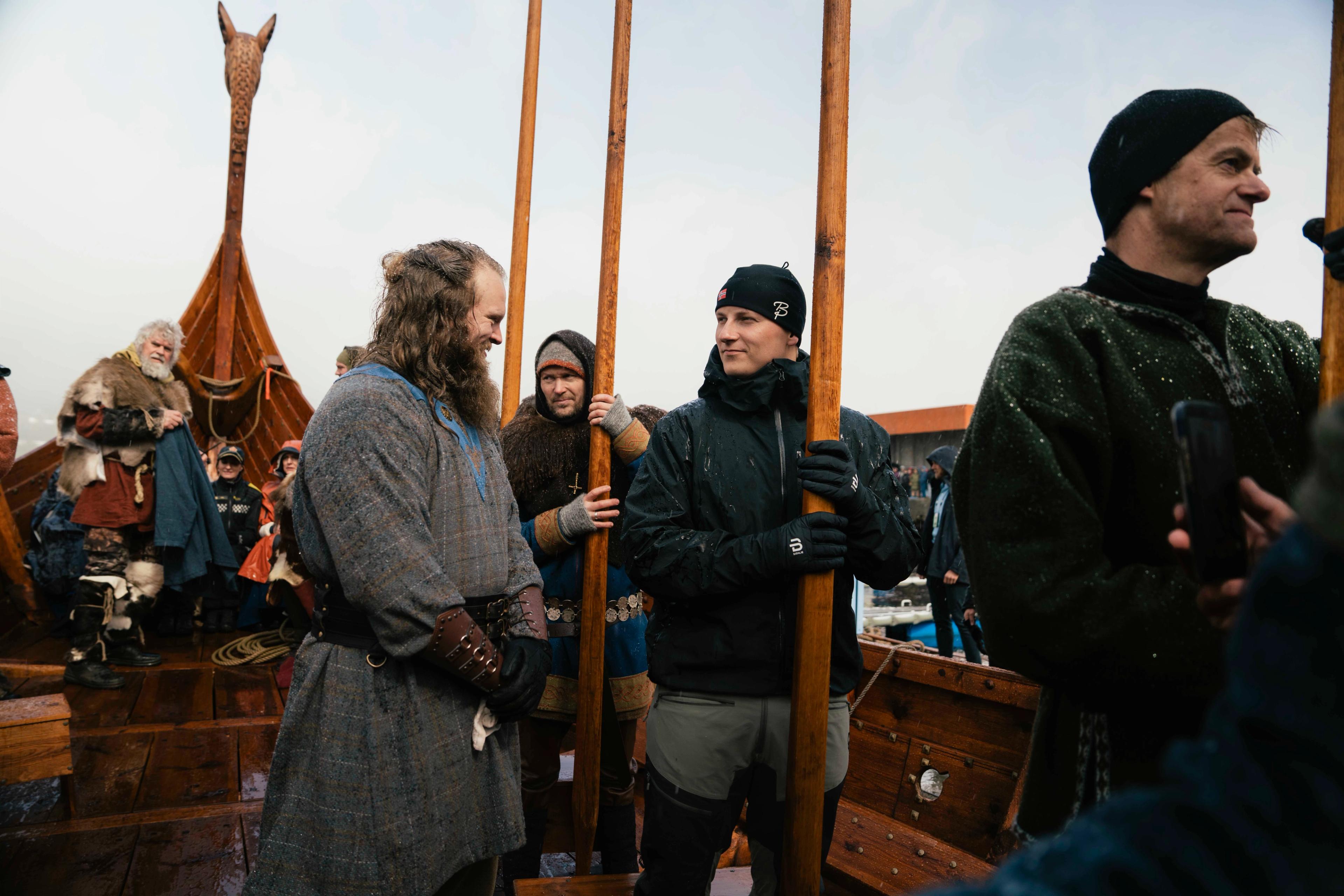 Prins Sverre Magnus står med en roåre i hendene ombord på et vikingskip. Rundt han står flere andre kledd i vikingklær med årer i hånda.