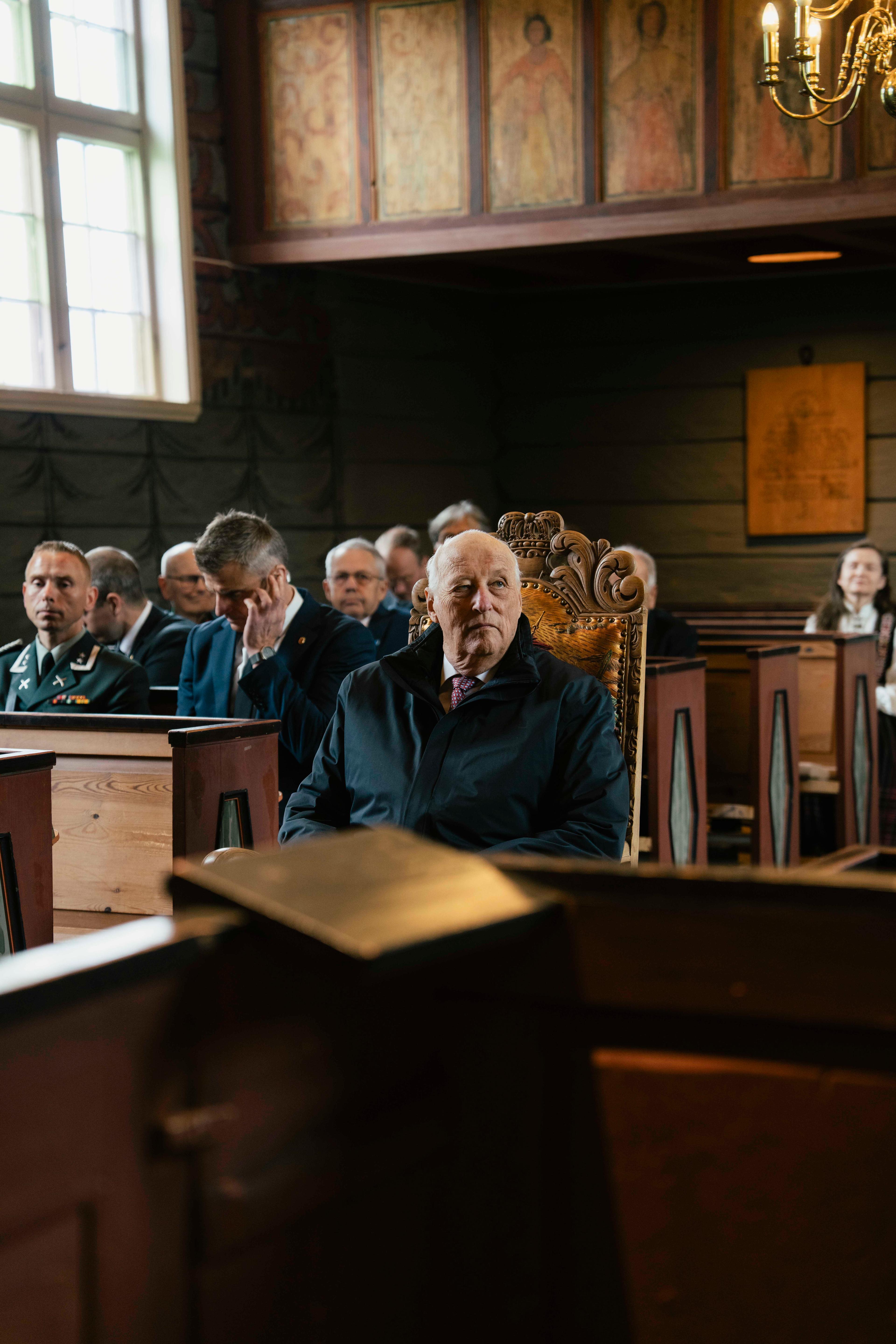 Kong Harald sit på ein stol mellom benkeradene.