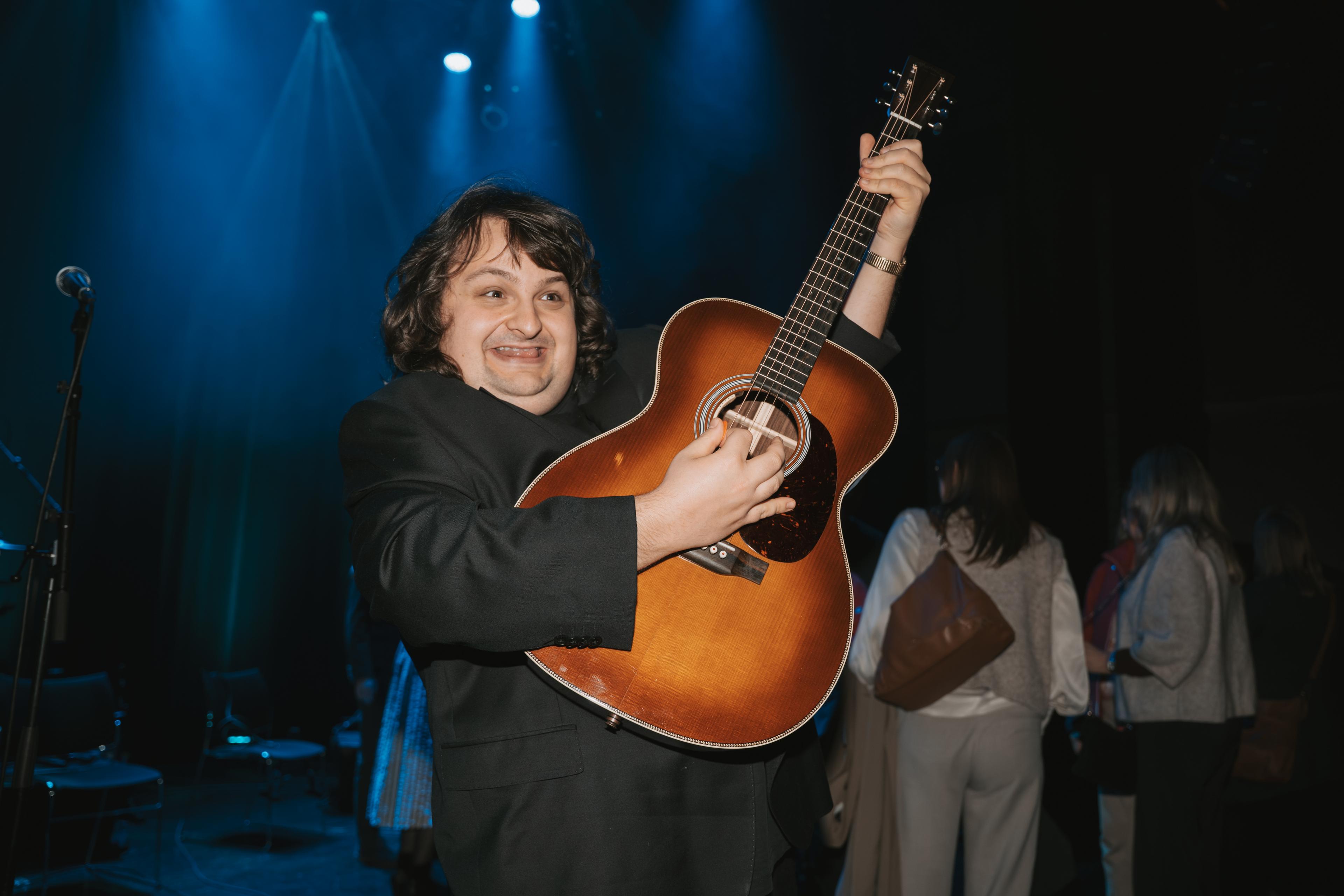 Konstantin held ein gitar høgt oppe og smiler breitt.