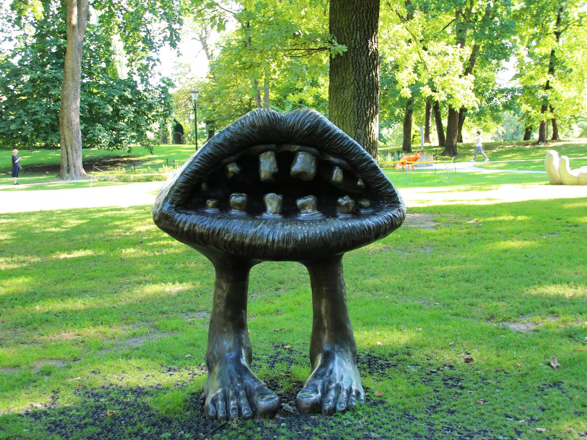 En stor munn, støpt i mørkt metall, står åpen med lepper og tenner står på egne ben i gresset.