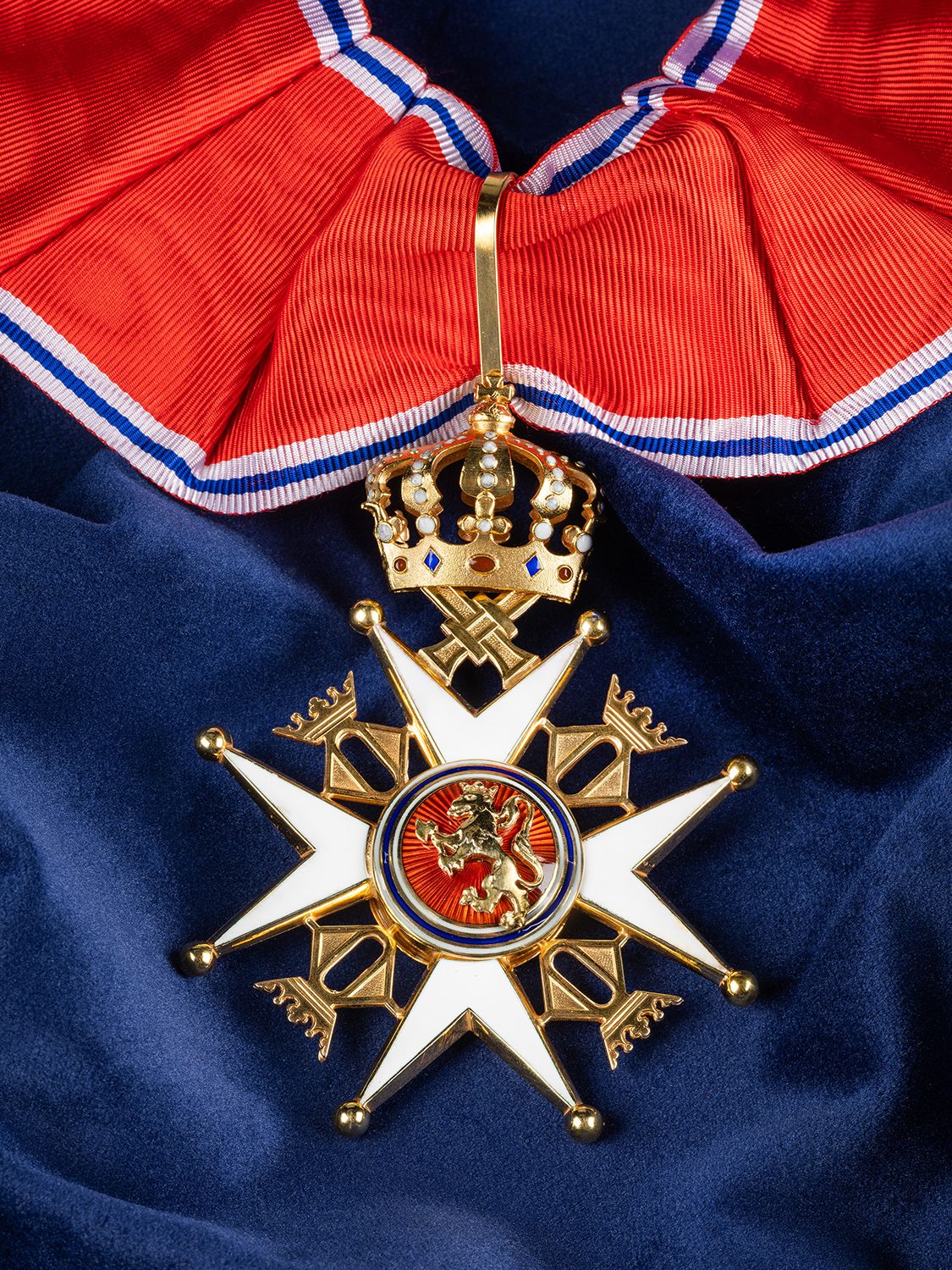 Nærbilde av ordensmerket festet i rødt bånd med blå og hvite striper på en bakgrunn av blått klede.