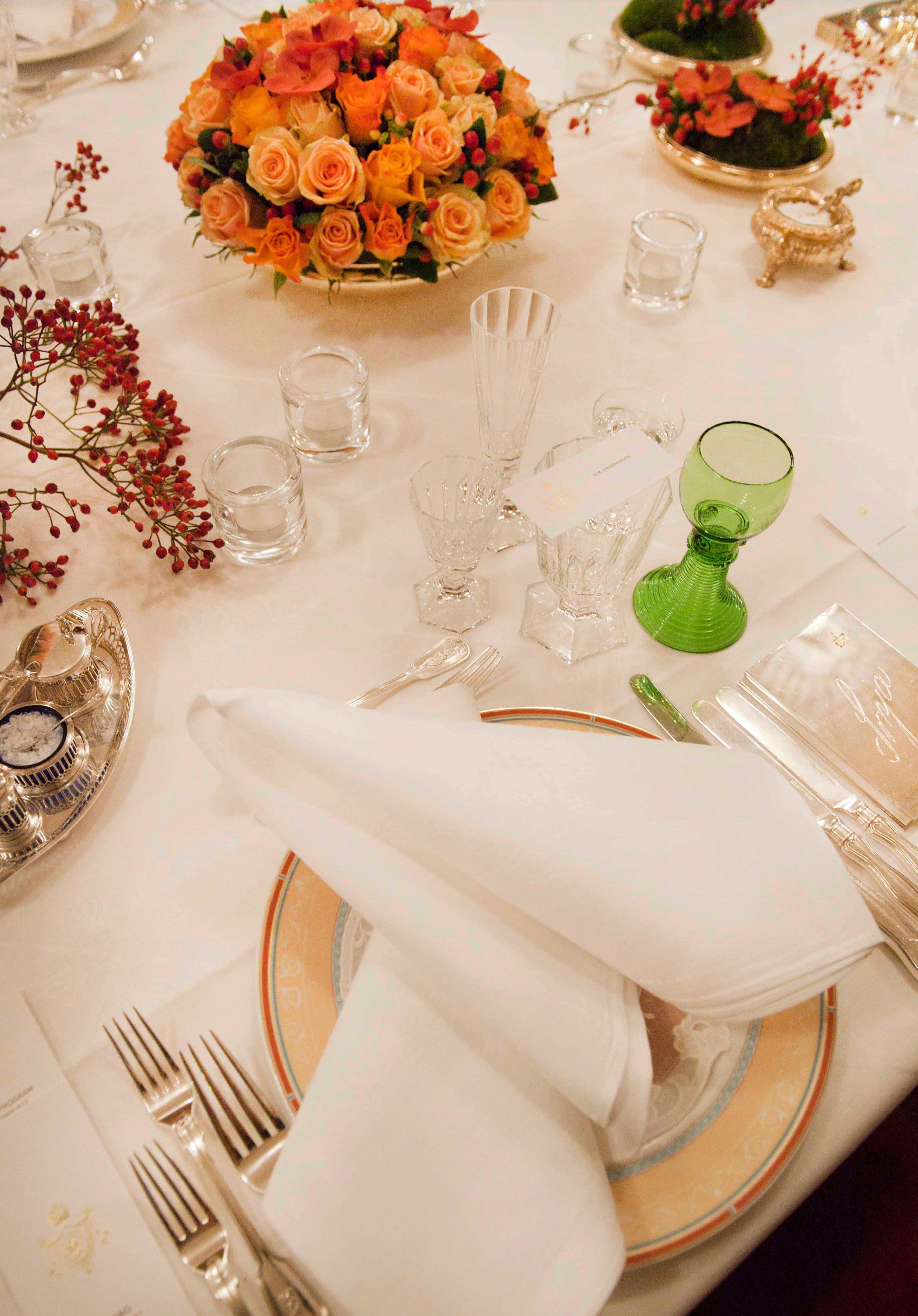 Nærbilde av en kuvert med dekketallerken, sølvbestikk og glass. Serviett og duk er i hvit damask.