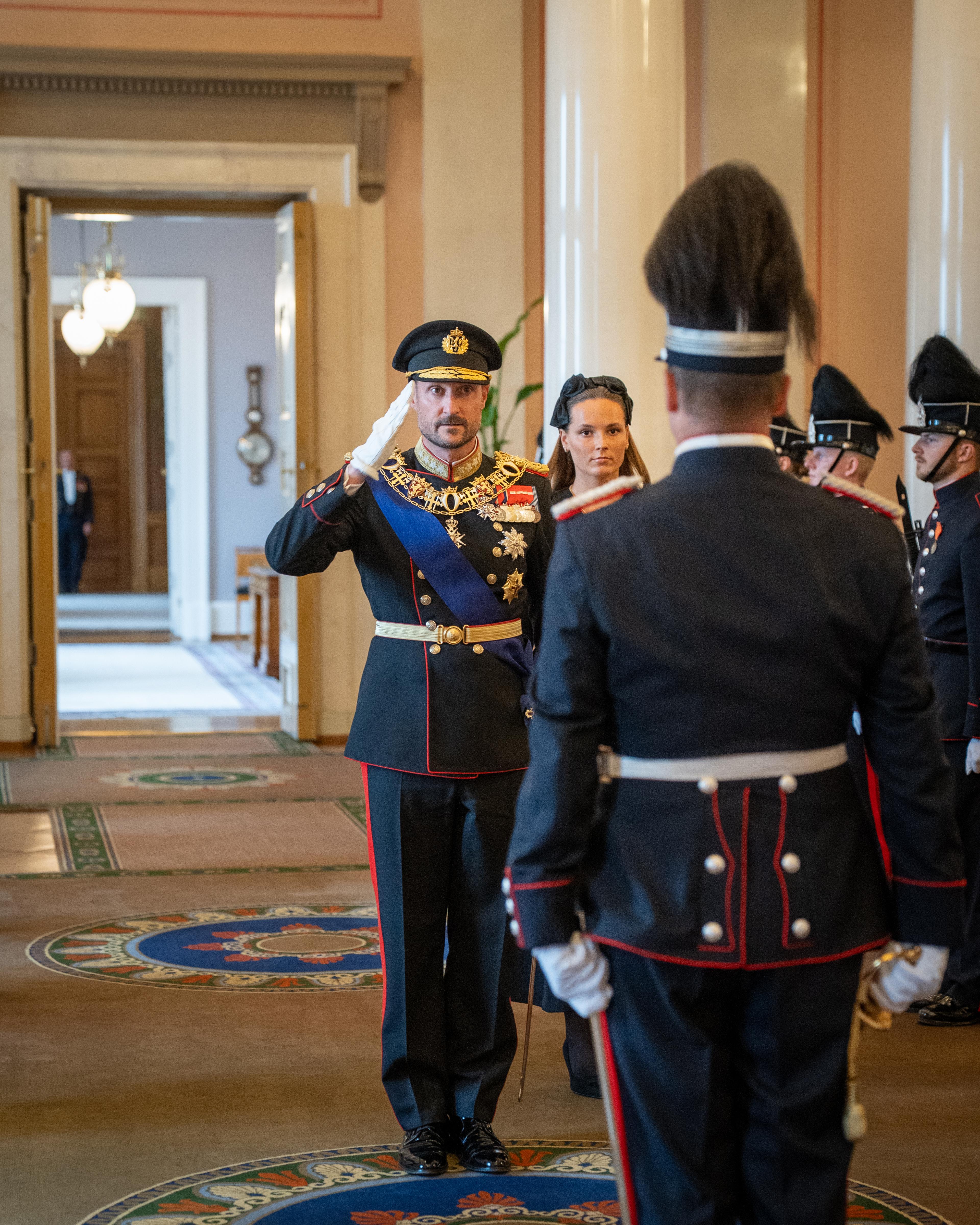 Kong Haakon hilser til sjef Krigsskolen. Kronprinsesse Ingrid Alexandra står bak Kongen.