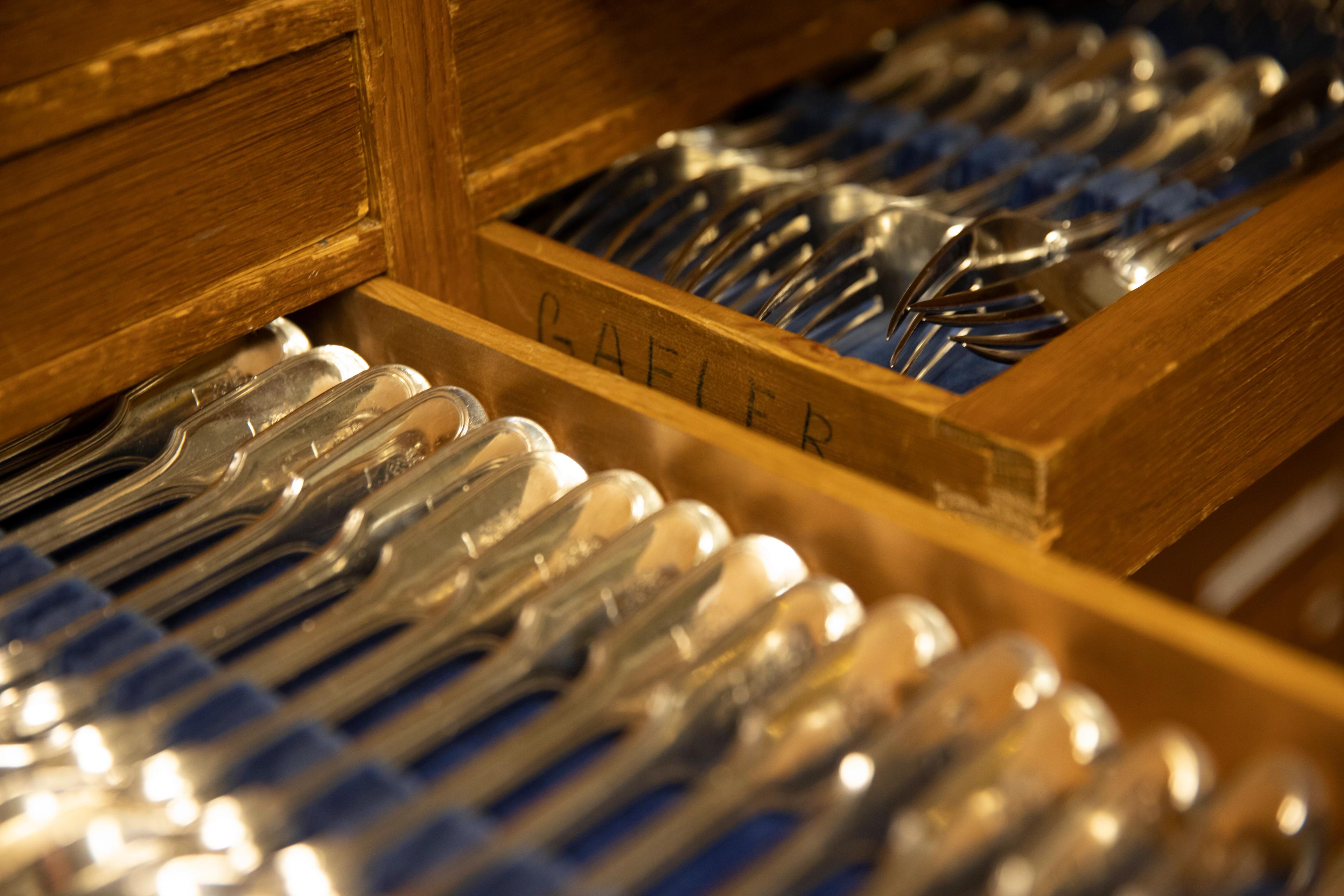 Nærbilde av sølvbestikk i oppbevaringsskuffer av tre med blått klede.