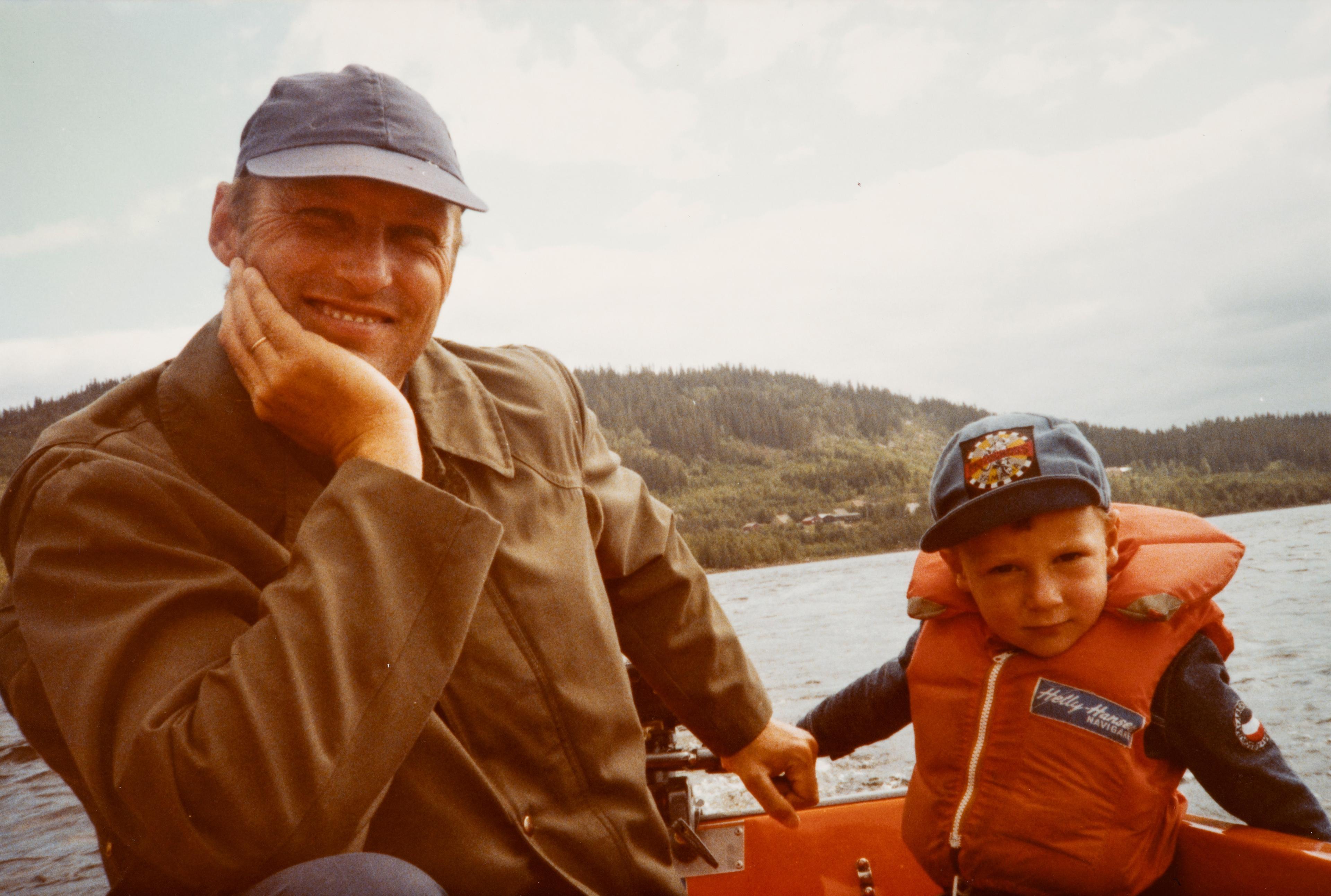 Far og sønn sitter i en liten motorbåt. Prins Haakon har redningsvest på.