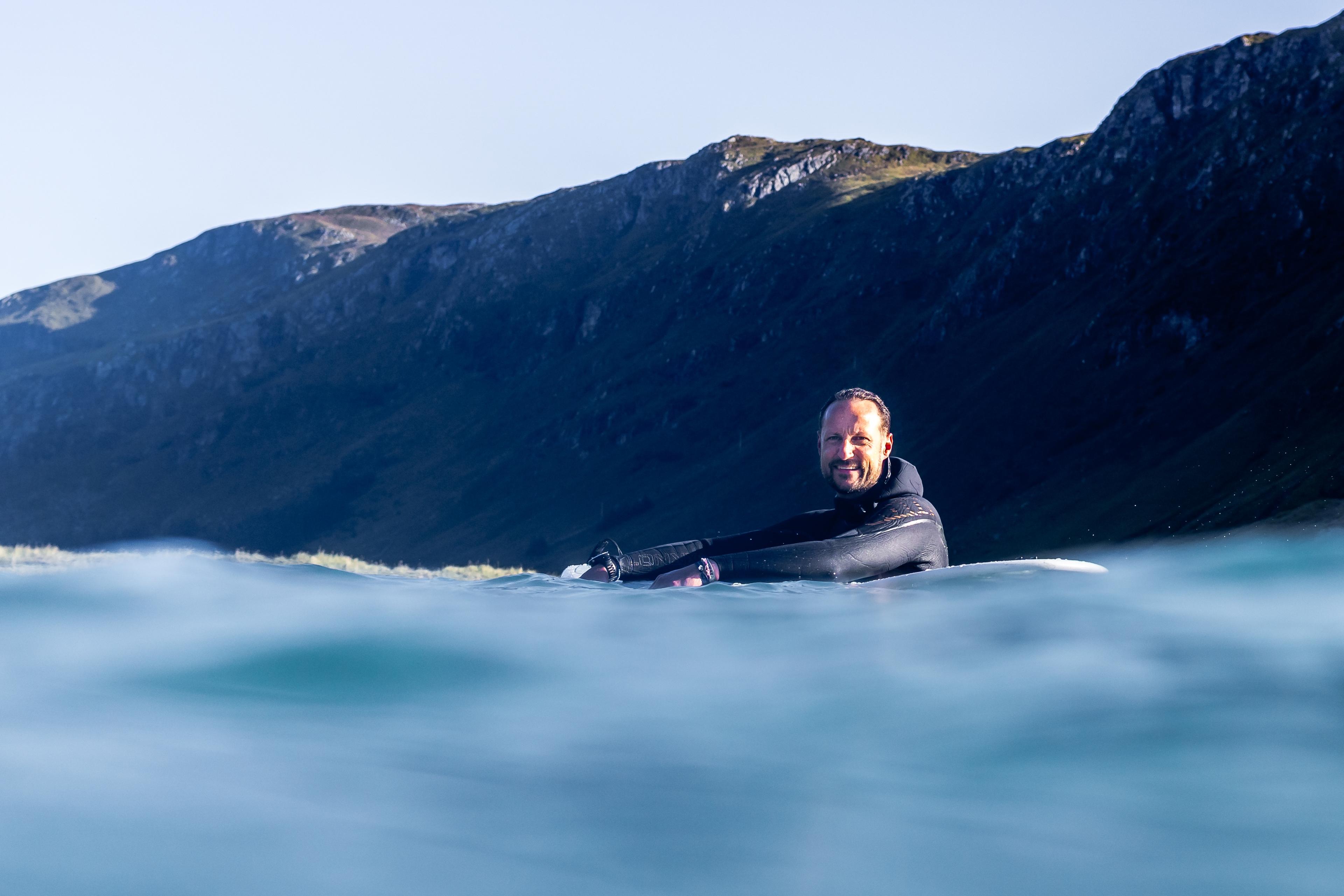 Smilende Kronprins Haakon hviler på surfebrettet ute på fjorden.