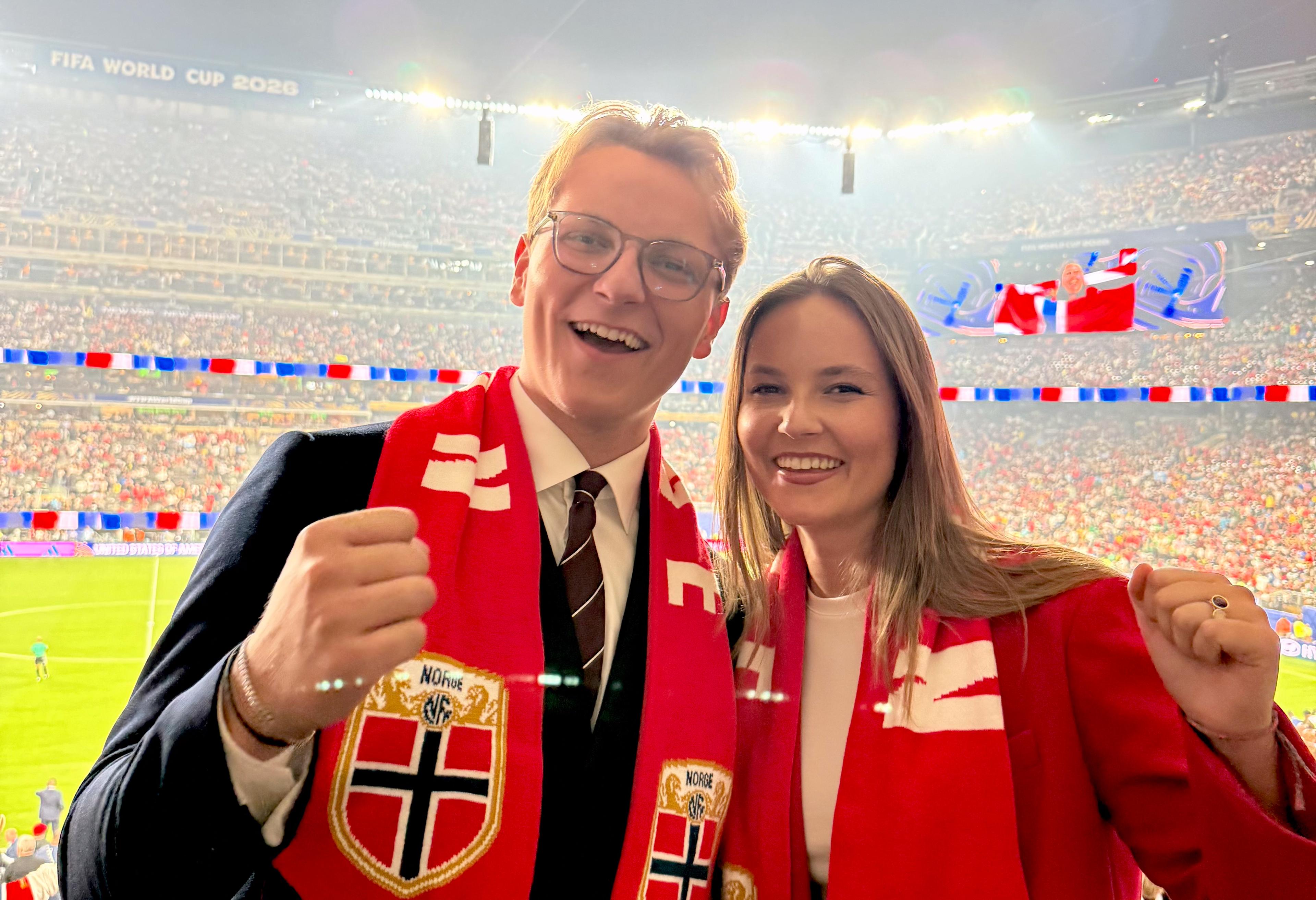 Prinsesse Ingrid Alexandra og Prins Sverre Magnus står sammen med norske fotballflagg rundt halsen. De smiler bredt og har en fotballstadion full av mennesker i rødt, hvitt og blått bak seg.