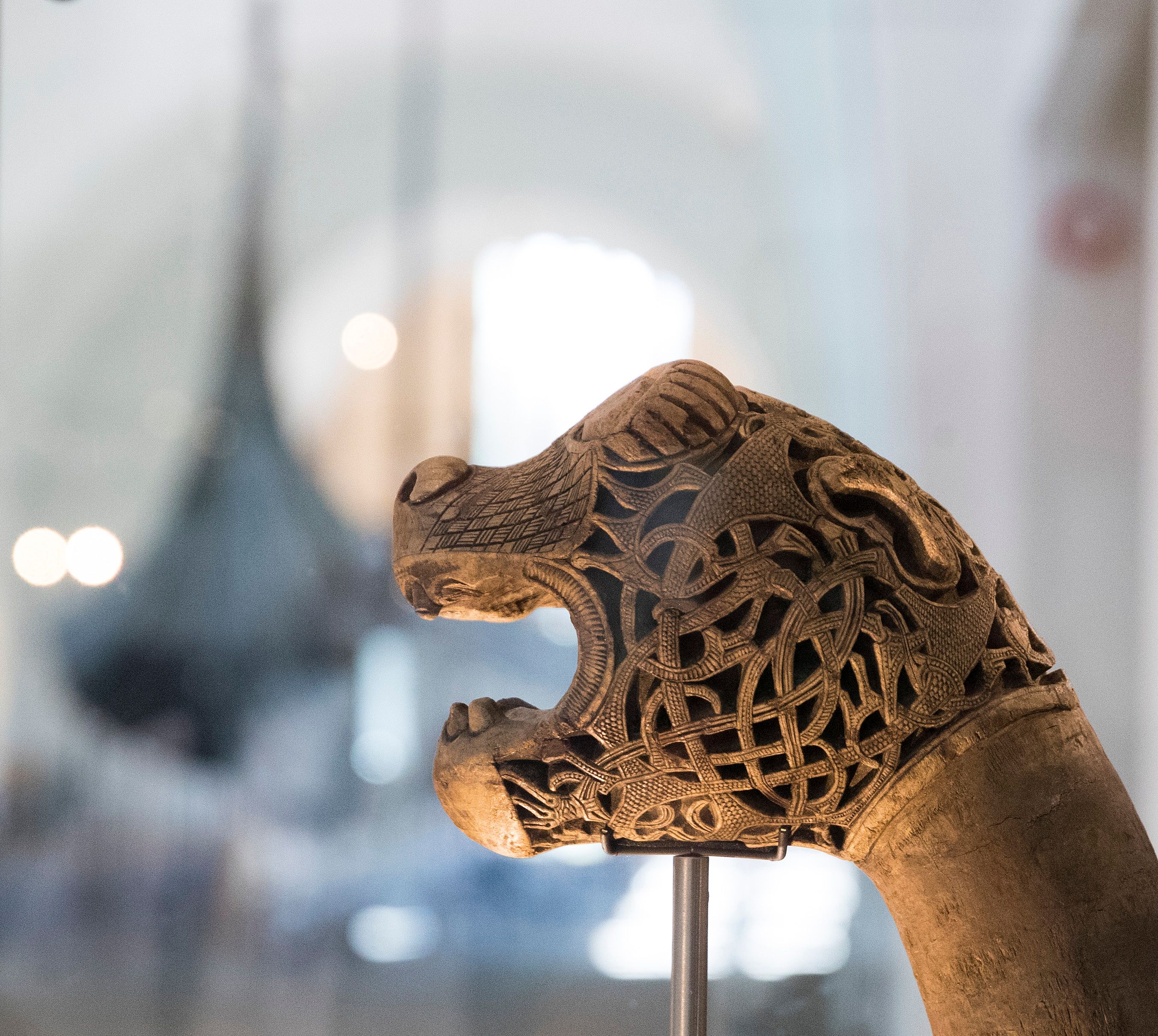 Et utskåret dragehode. Gokstadskipet i bakgrunnen.