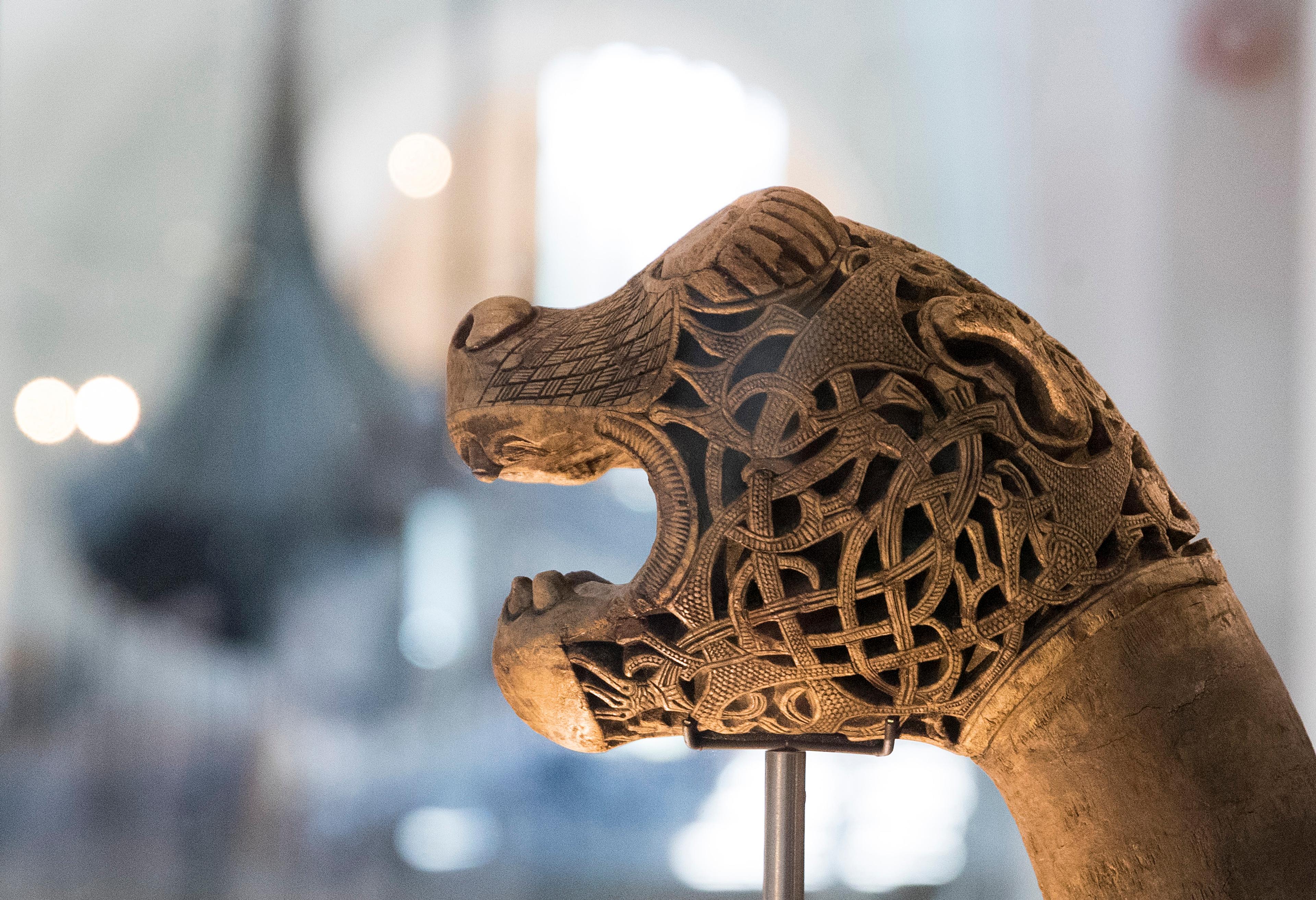 Et utskåret dragehode. Gokstadskipet i bakgrunnen.