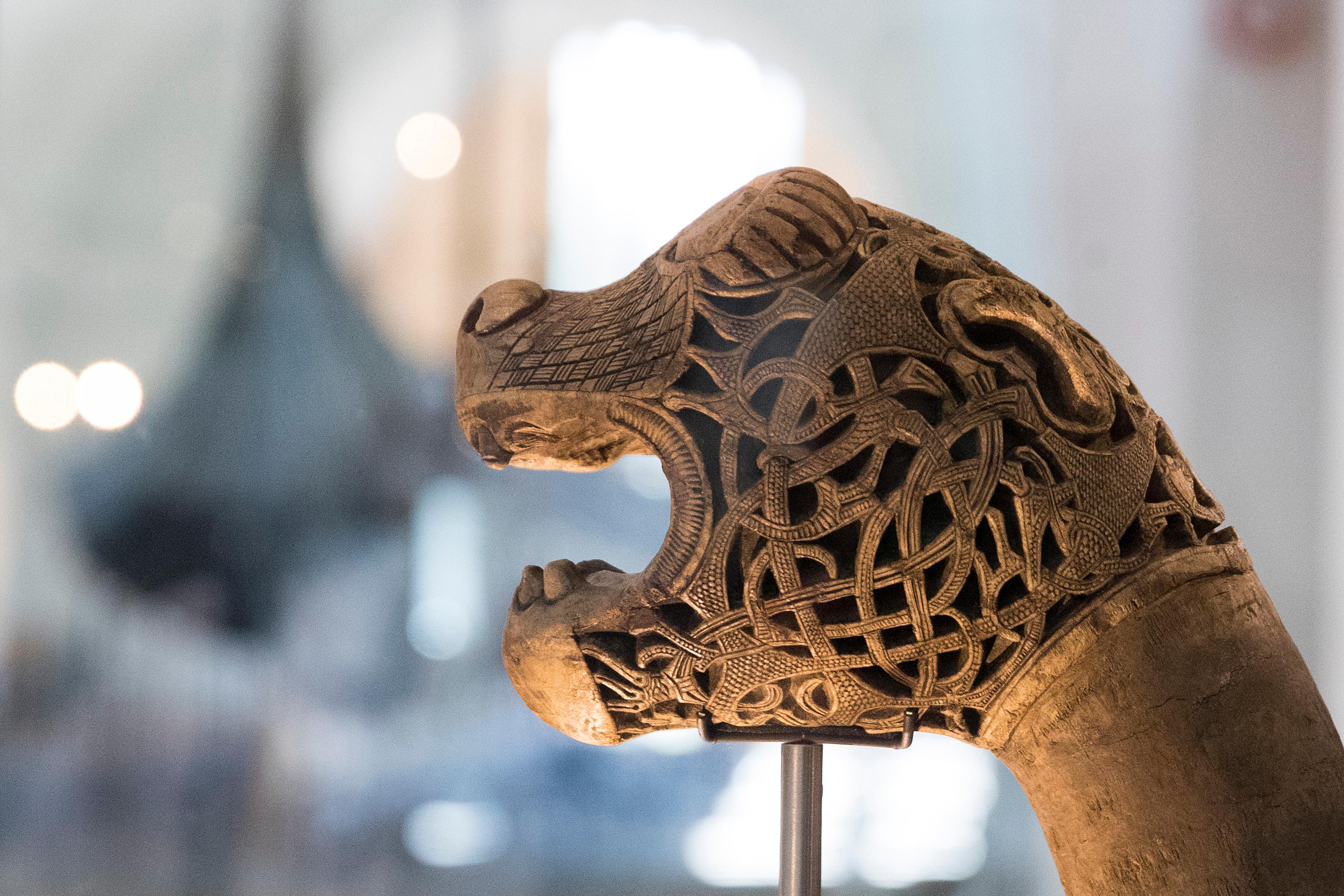 Et utskåret dragehode. Gokstadskipet i bakgrunnen.