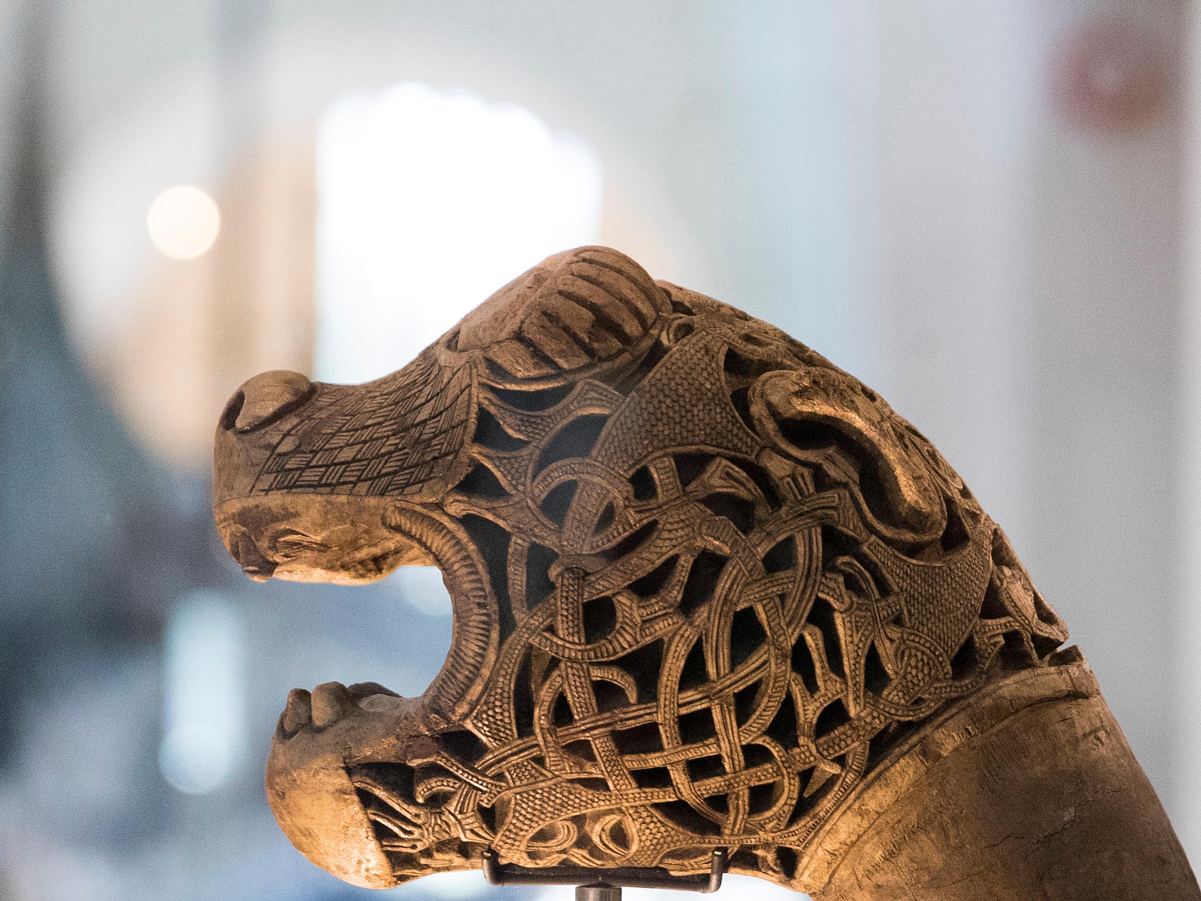 Et utskåret dragehode. Gokstadskipet i bakgrunnen.