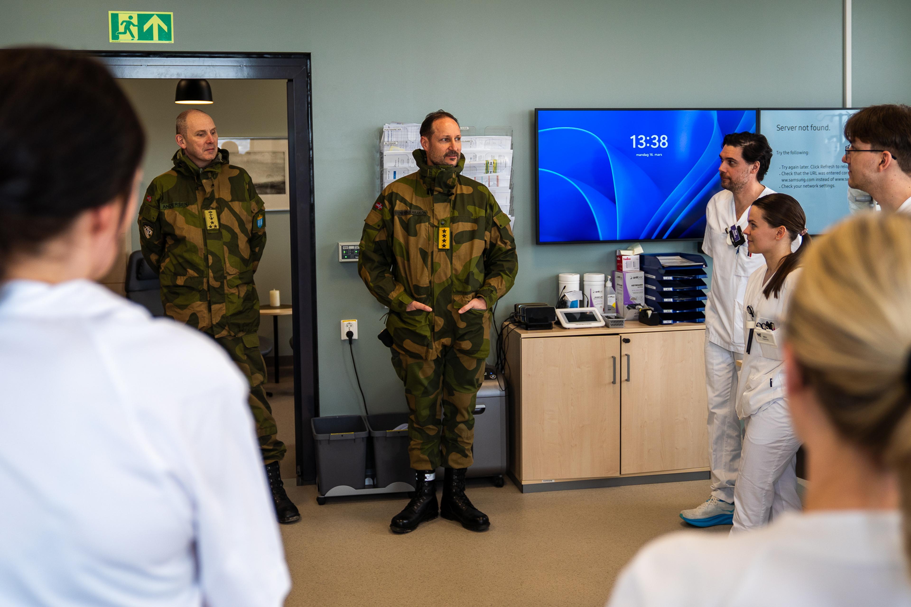 Kronprins Haakon, ikledd feltuniform, i samtale med helsepersonell.