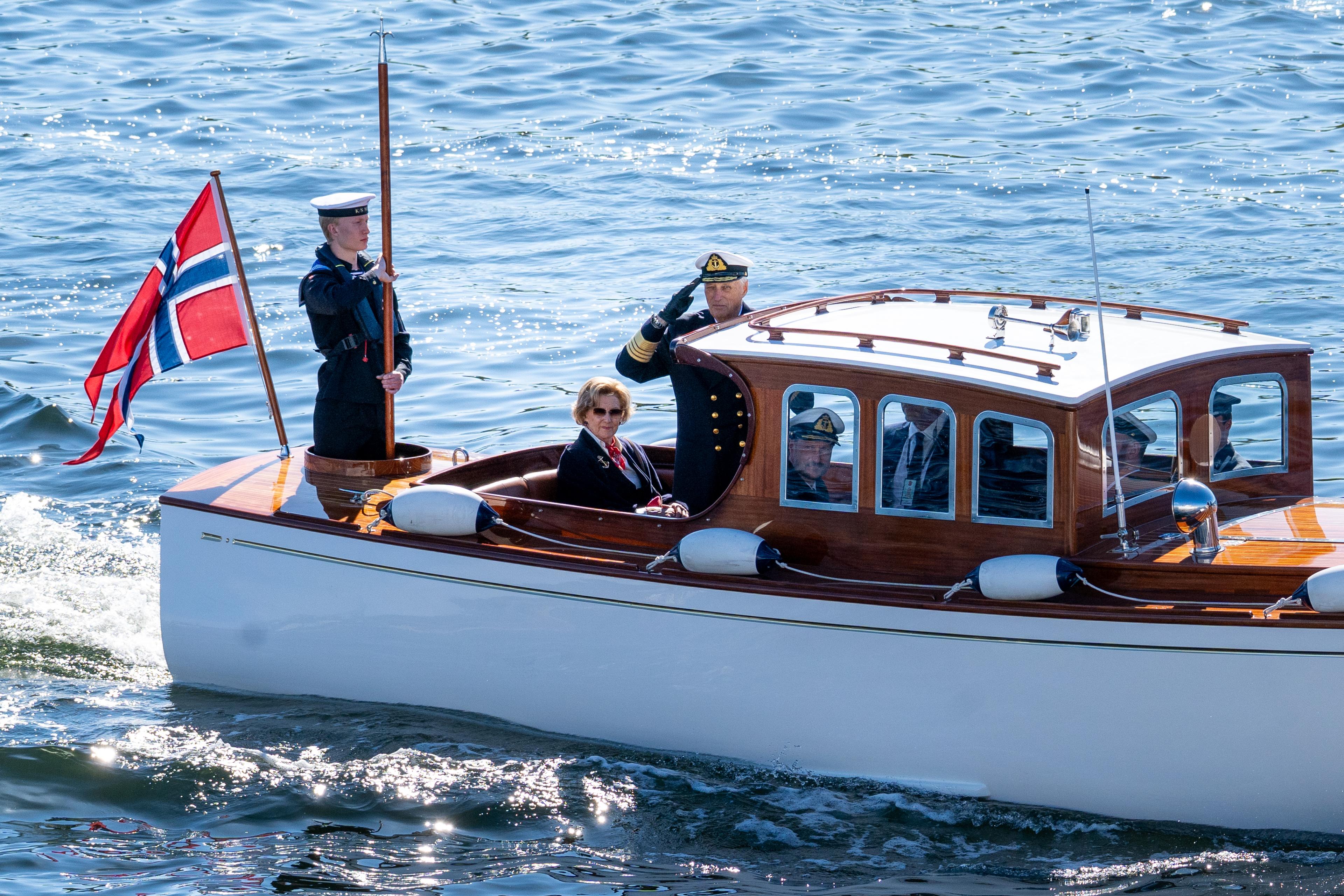 Kong Harald står med handa til hua, medan Dronning Sonja og Kronprins Haakon sit.