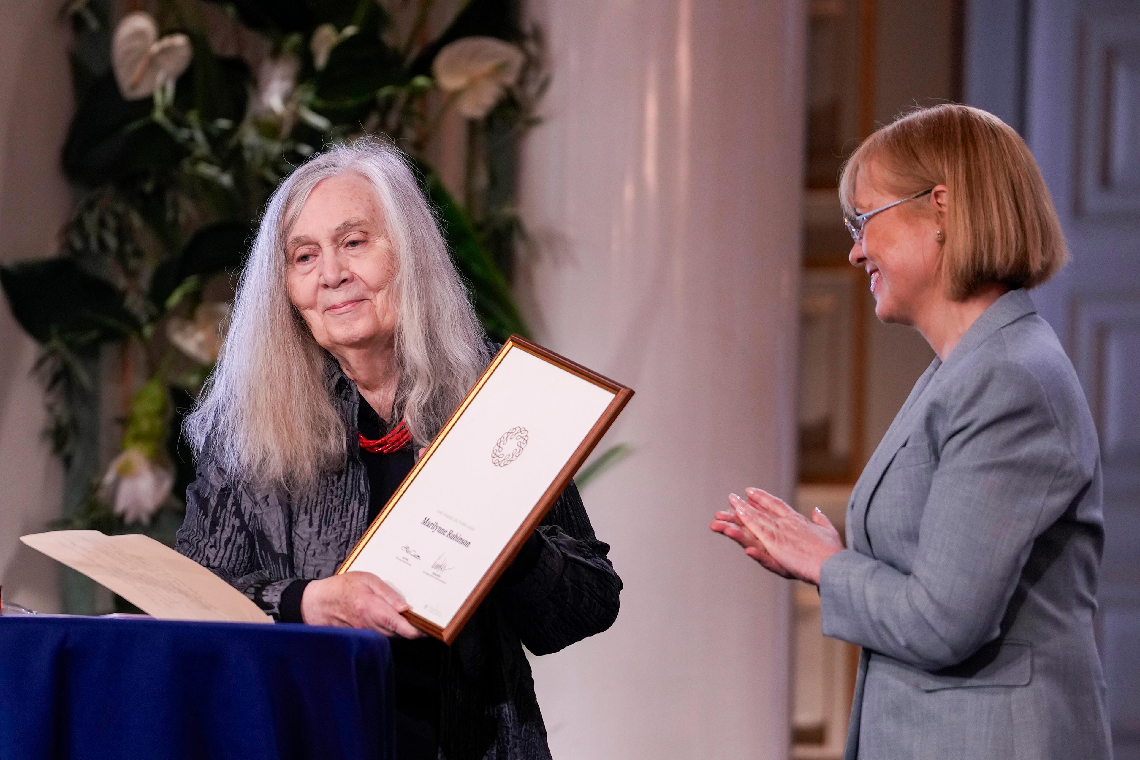 Robinson smilende med det innrammede diplomet i hendene. Wetås står ved siden av henne og klapper.