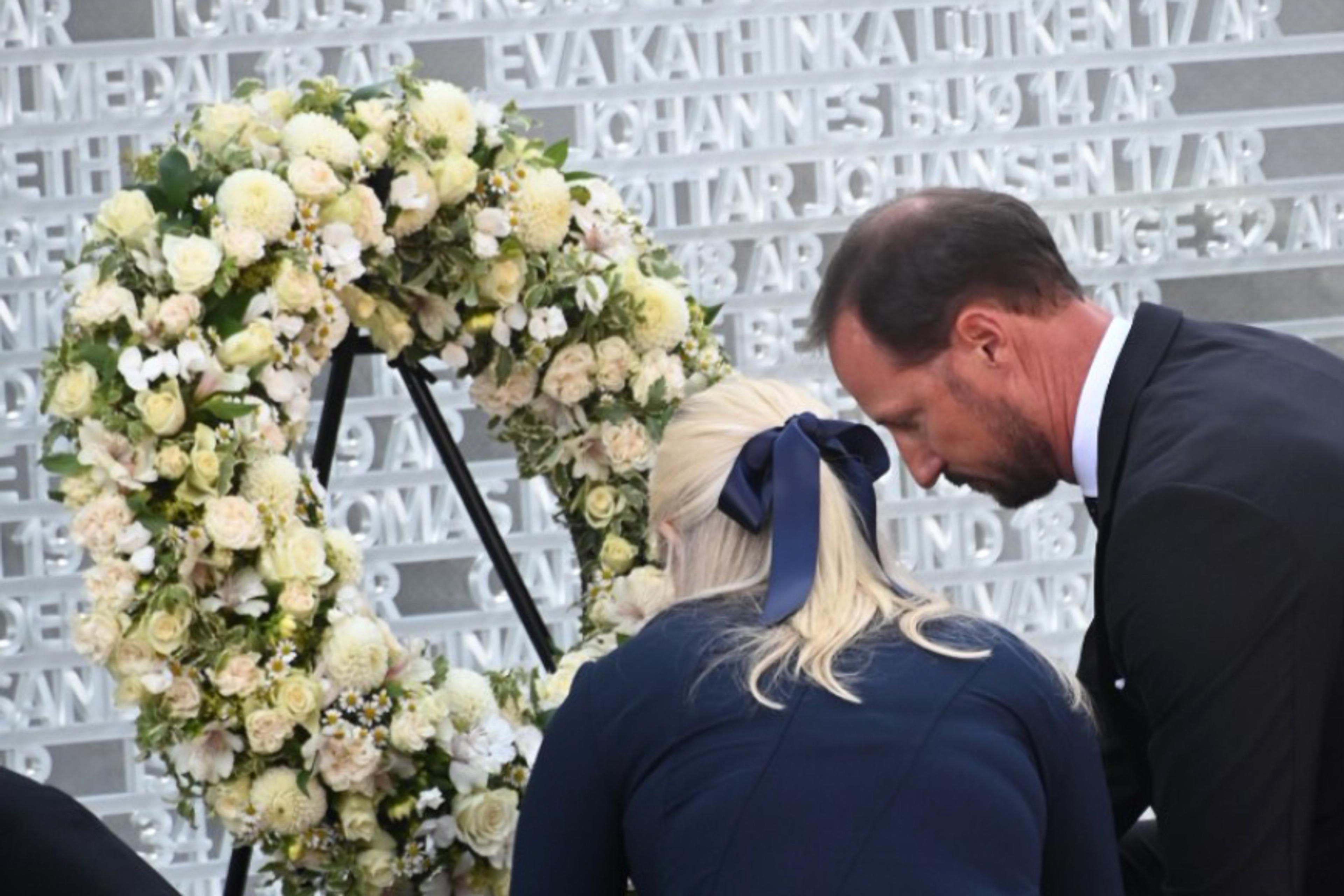 Kronprinsparet sitter på huk foran en stor krans med hvite blomster og tavlen med navnene.