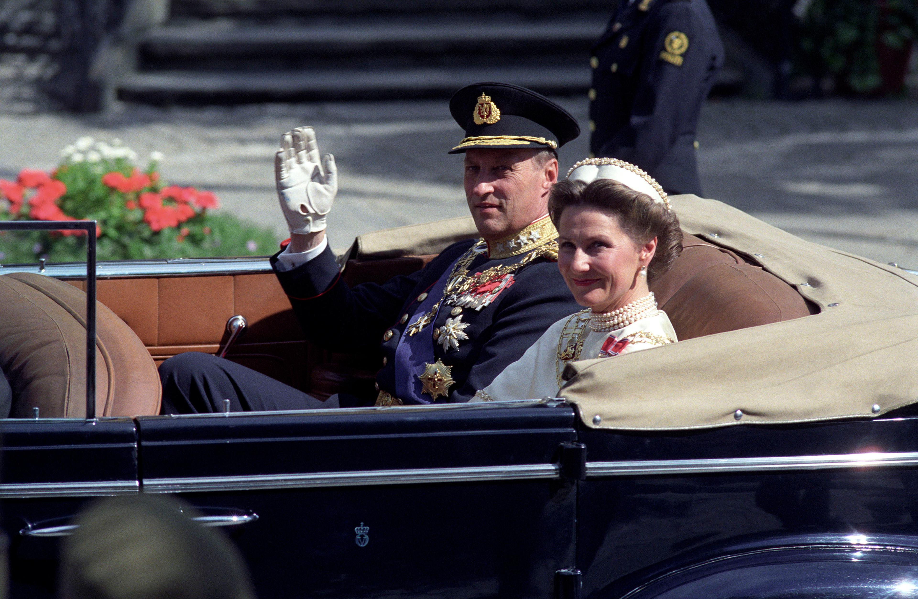 Kongen og Dronningen i åpen bil. Kong Harald i gallauniform, Dronningen i sin hvite kroningskjole. Kongen vinker.