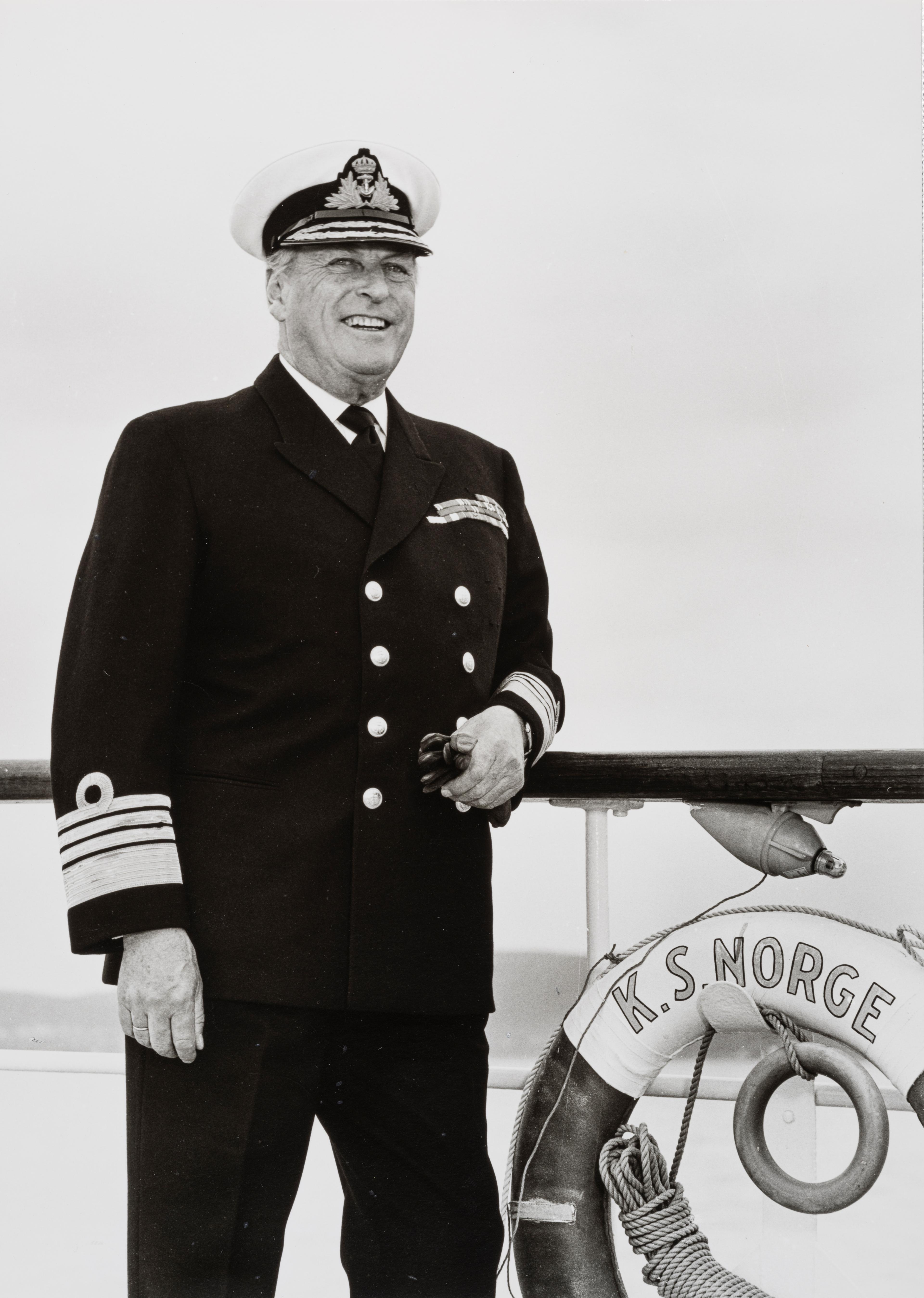 Kong Olav står ved rekka i marineuniform.