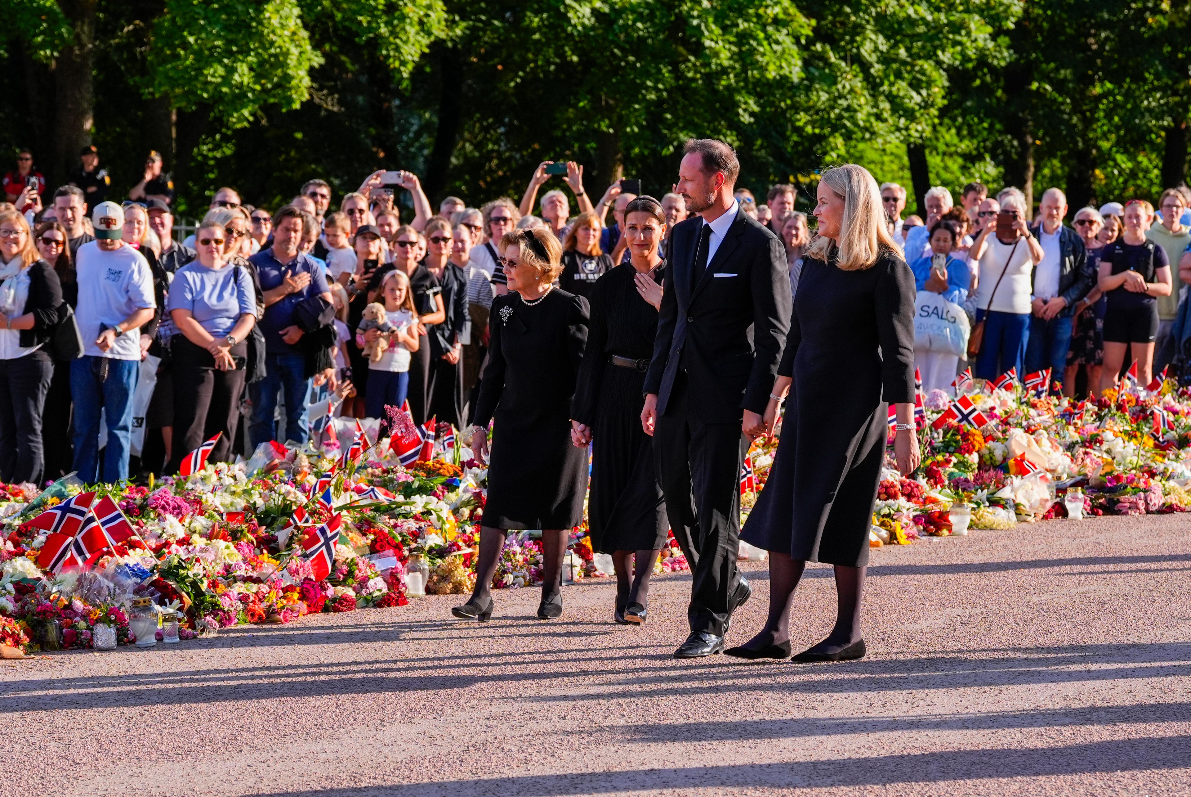 Kongen og Dronningen, Dronning Sonja og Prinsesse Märtha Louise går sortkledde sammen langs blomsterhavet.