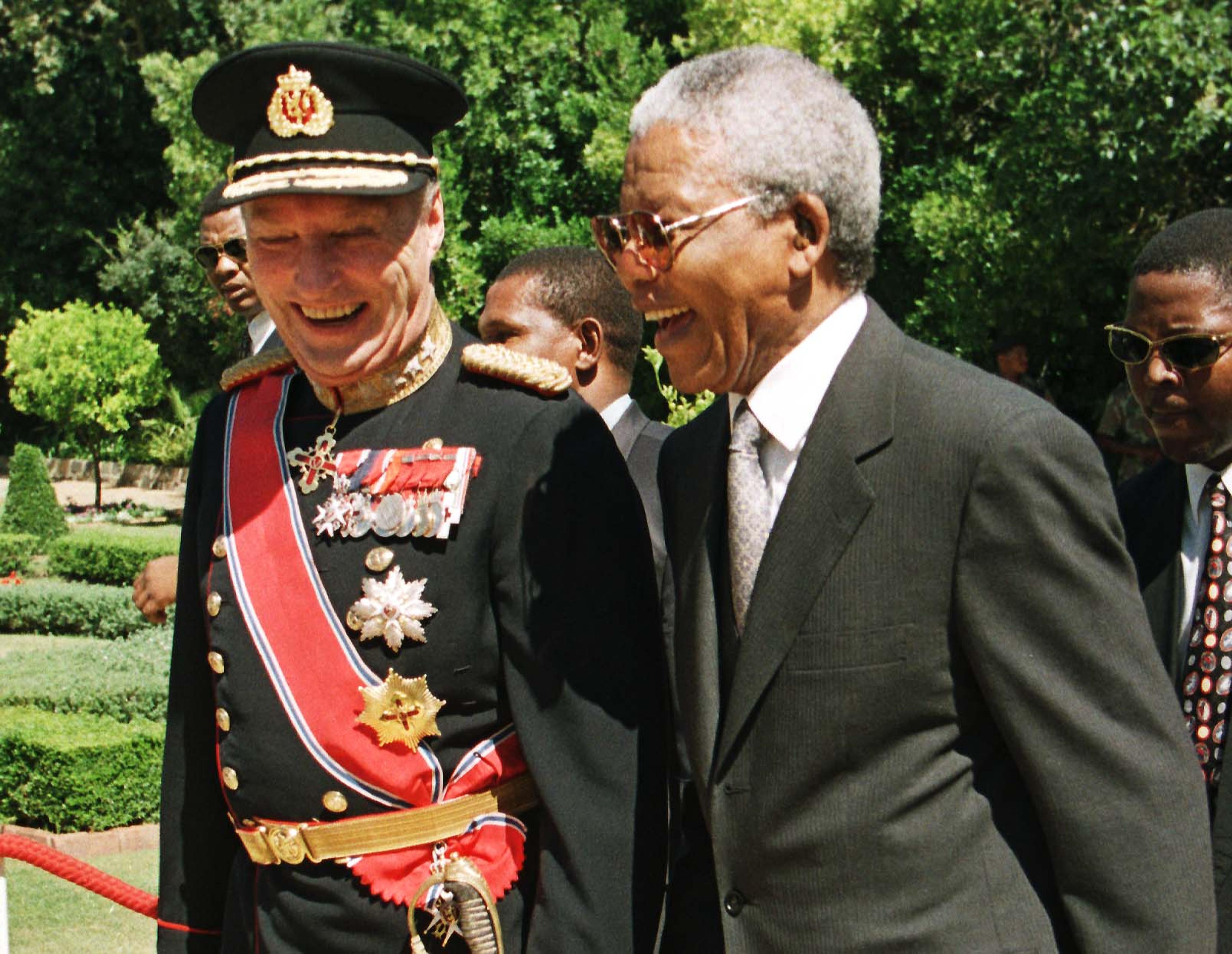Kong Harald og Nelson Mandela ler mens de går sammen i Cape Town.