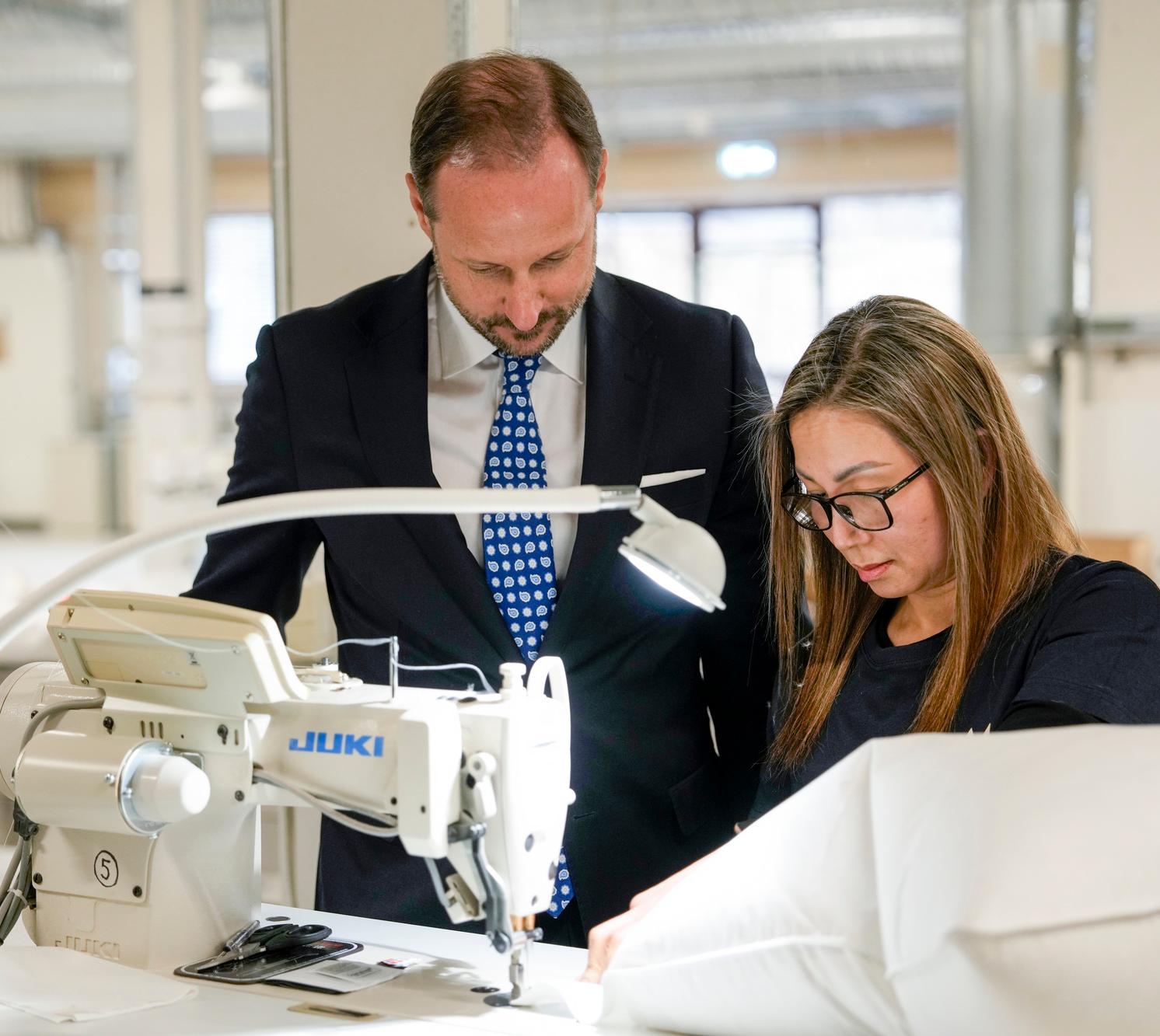 Kronprins Haakon står bøyd over en symaskin sammen med en medarbeider hos Norsk Dun.