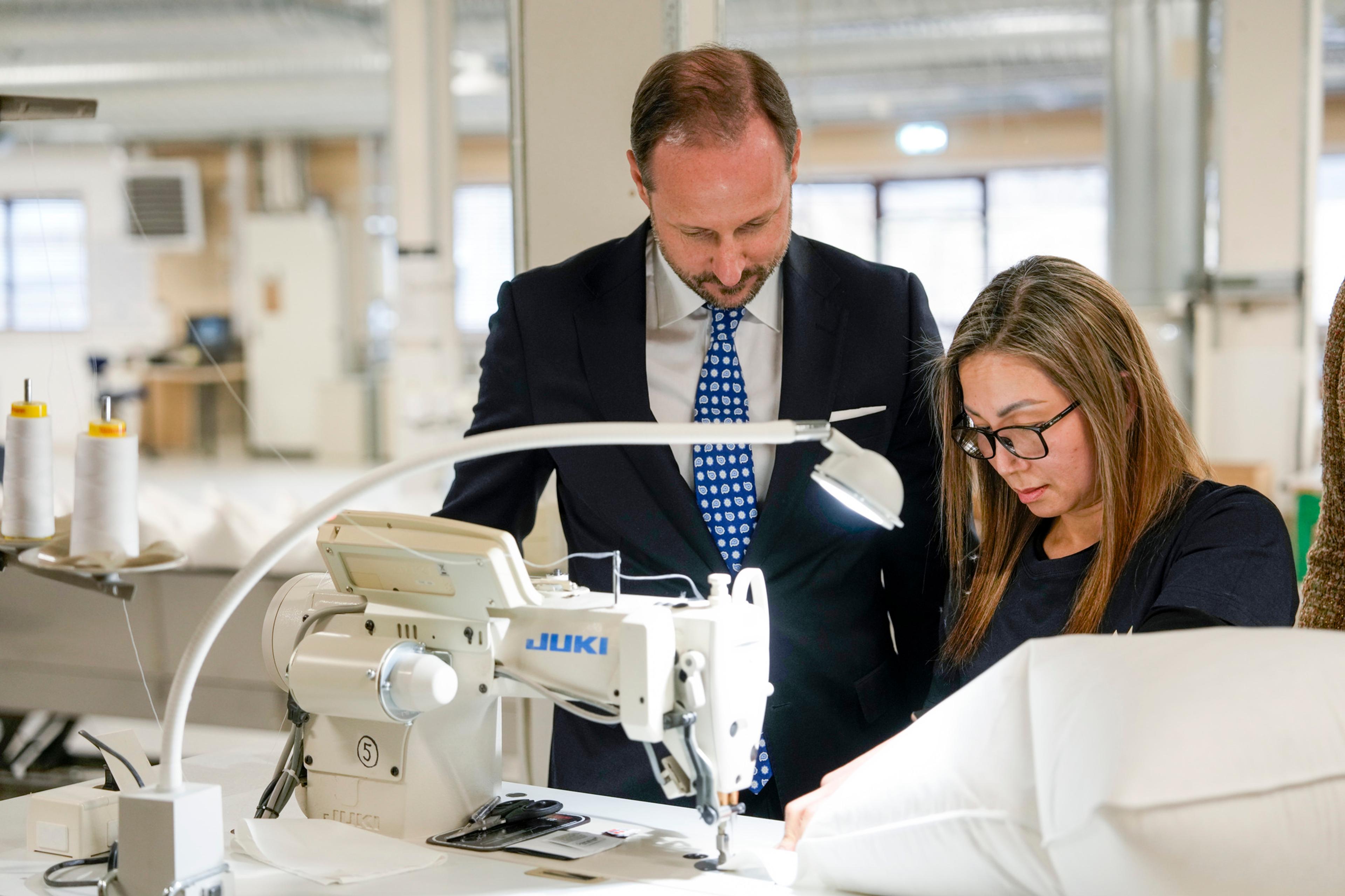 Kronprins Haakon står bøyd over en symaskin sammen med en medarbeider hos Norsk Dun.