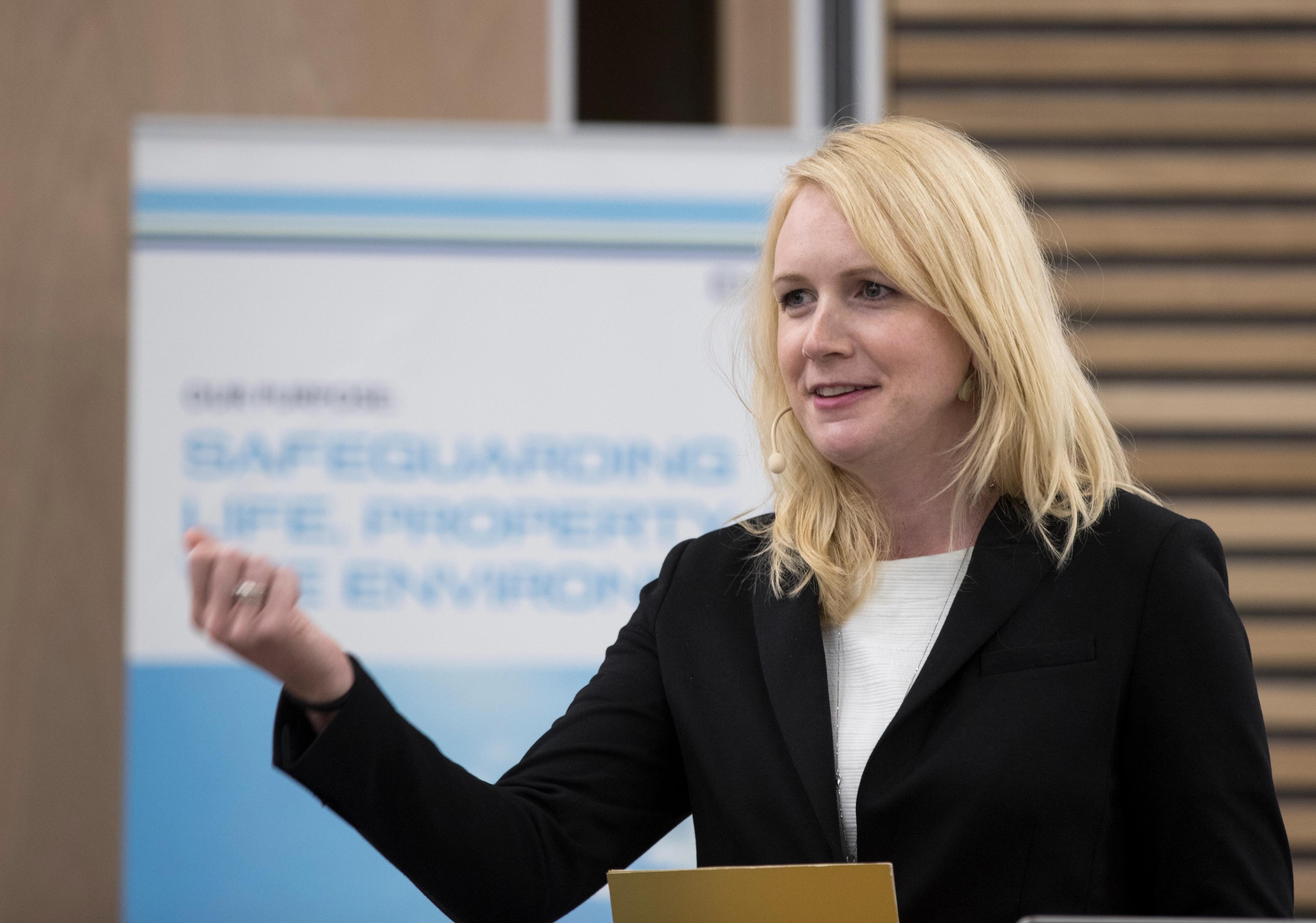 Lystrup snakker foran en skjerm med bilde av rapportens forside.
