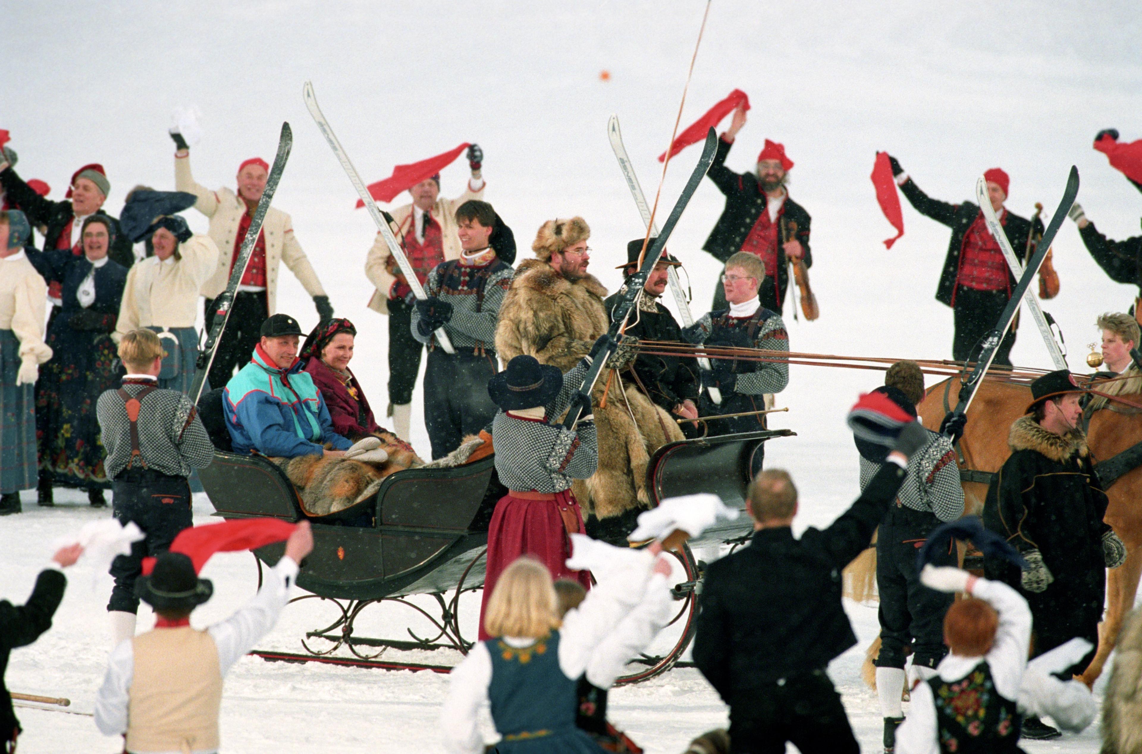 Kongeparet sitter i en slede og mennesker vinker på hver side
