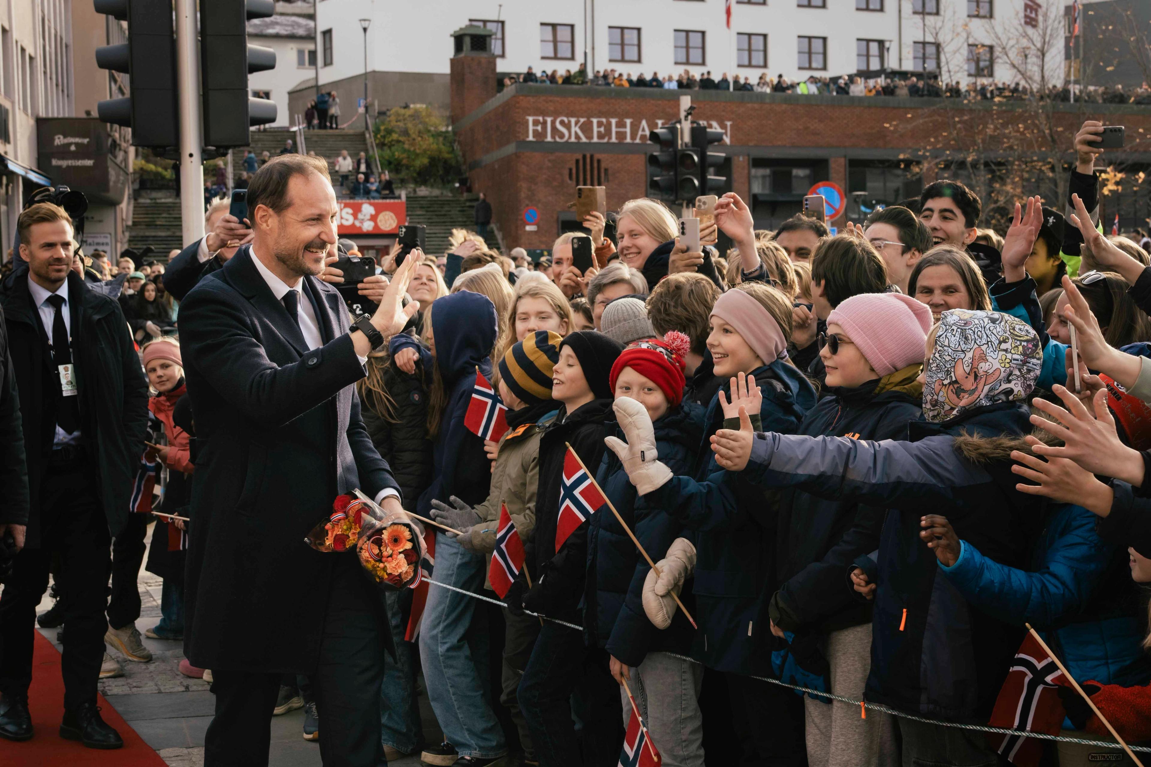 En smilende konge hilser "high five" med barn på plassen.