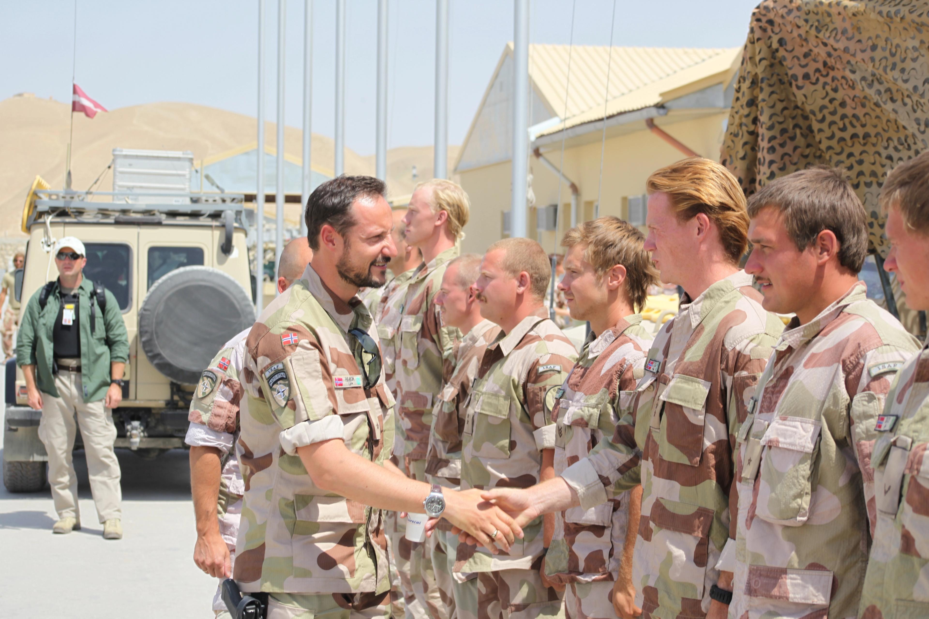 Kronprinsen i uniform håndhilser på en rekke soldater som står foran ham.