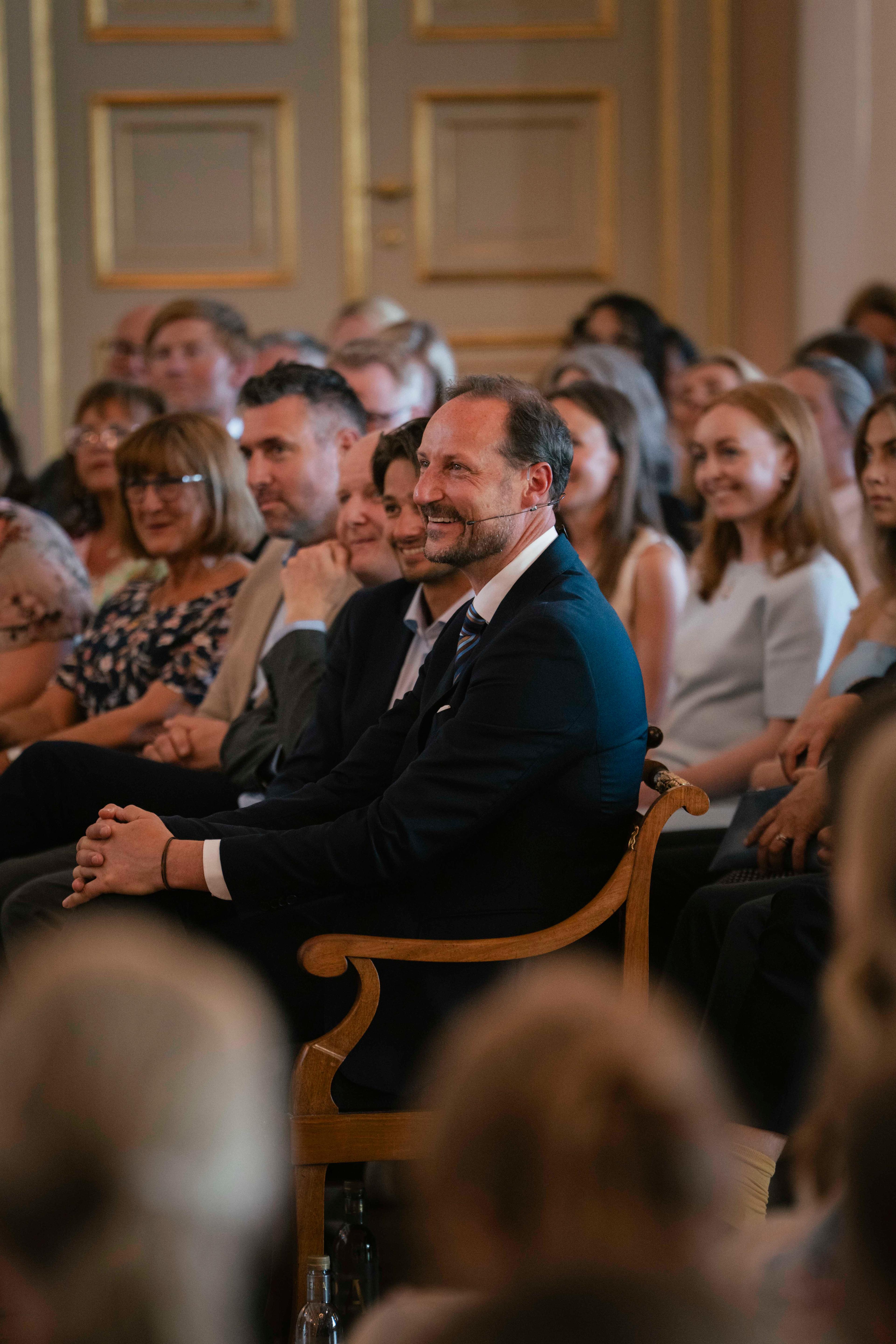 Kronprinsen sitter smilende blant publikum og følger med på det som skjer på scenen.