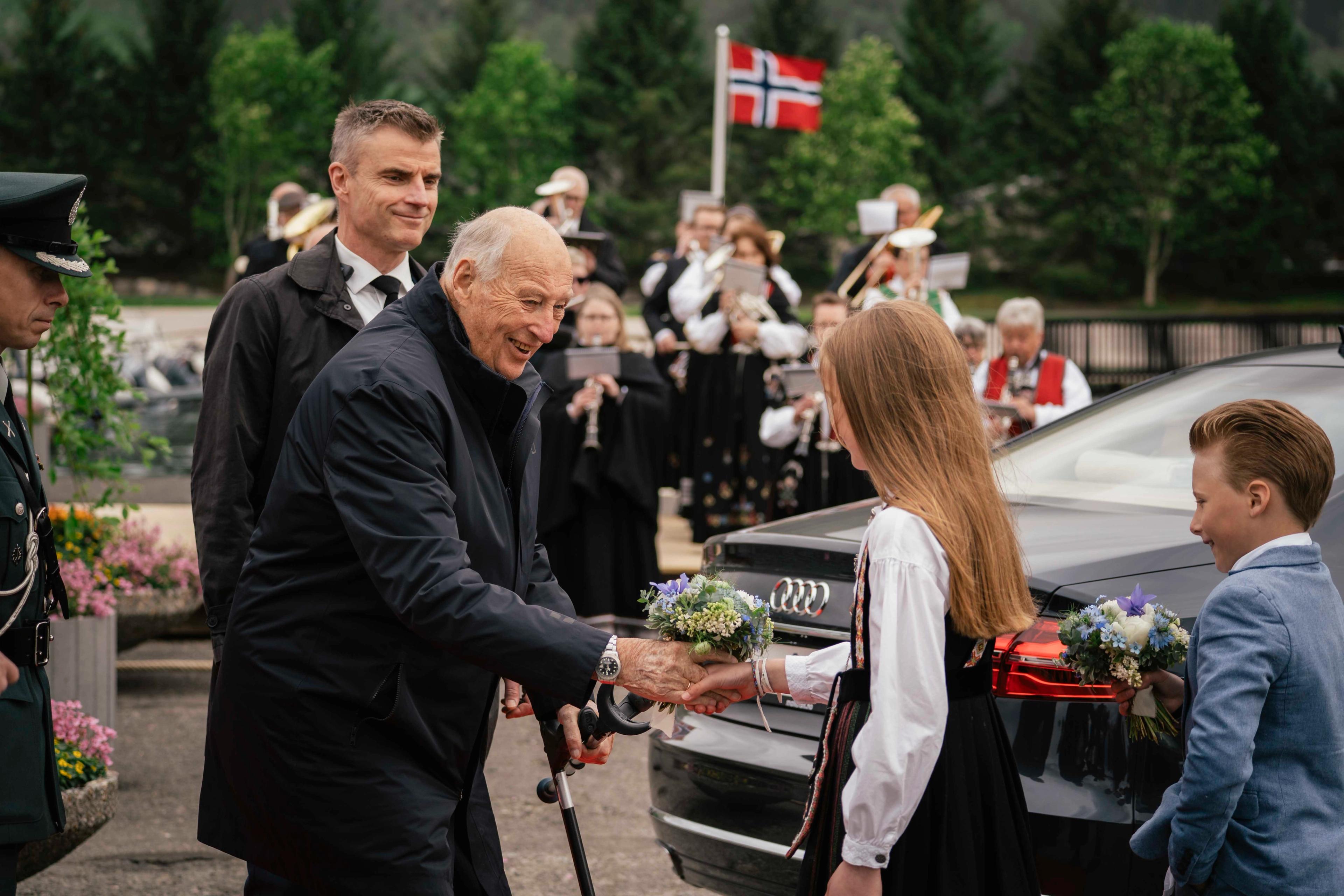 Kong Harald tar imot blomar av Maja, medan Einar står klar med sine blomar.