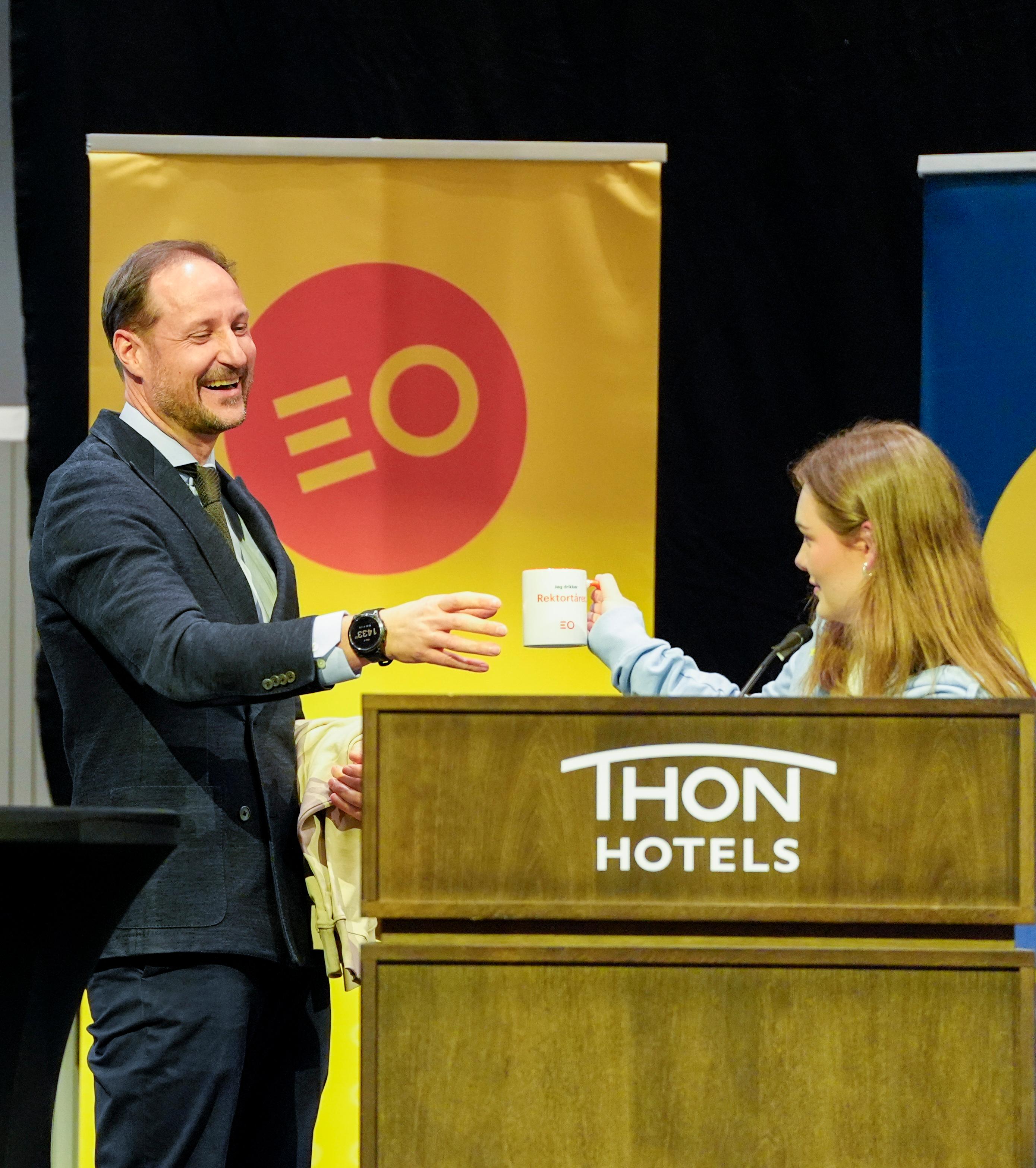 Kronprins Haakon ler medan han tek imot ein kopp med påskrifta «Eg drikk rektortårer».