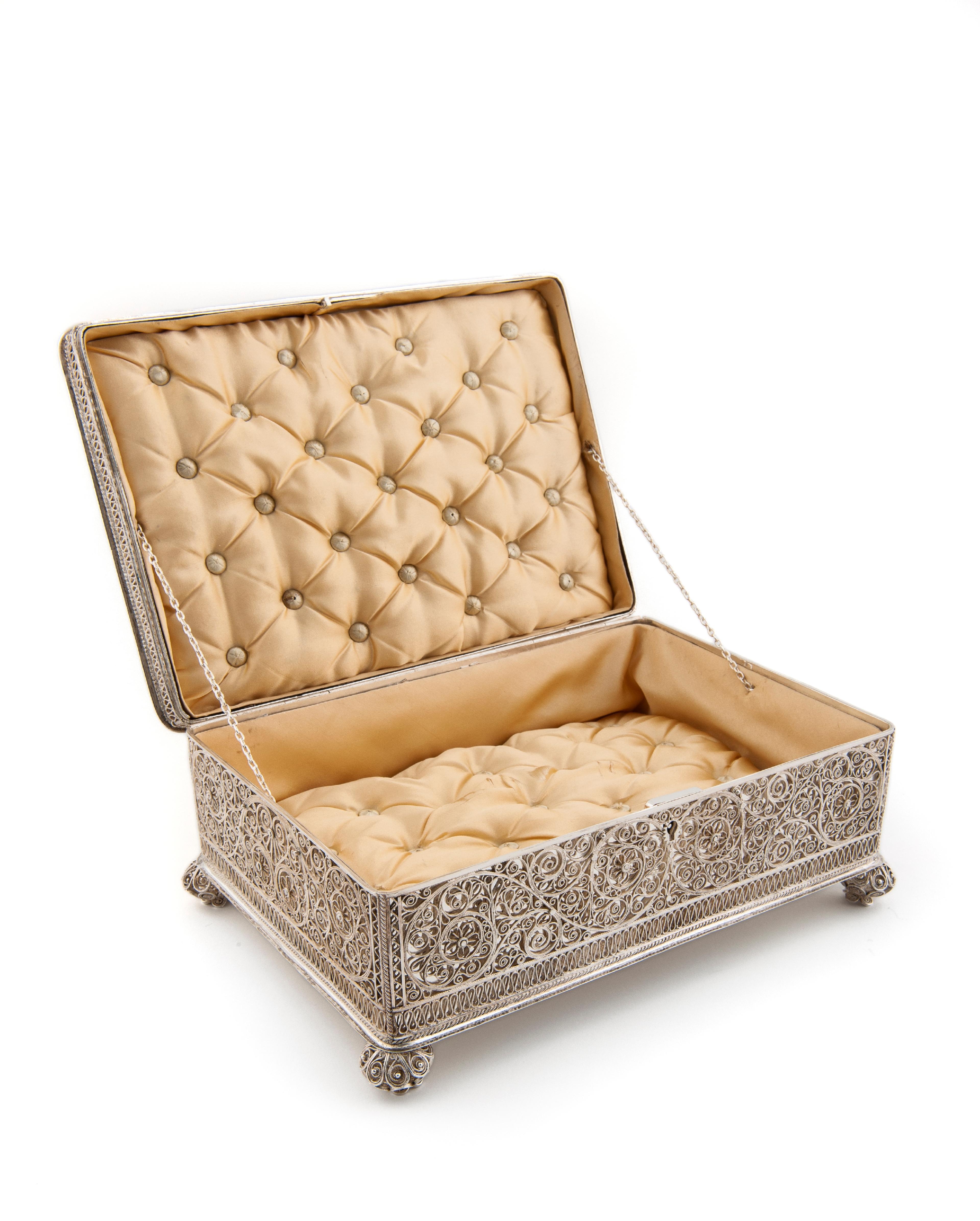 Sølvskrinet står med lokket åpent. Innvendig er det polstret med gyllent, mykt stoff. Et intrikat filigransmønster pynter utsiden.