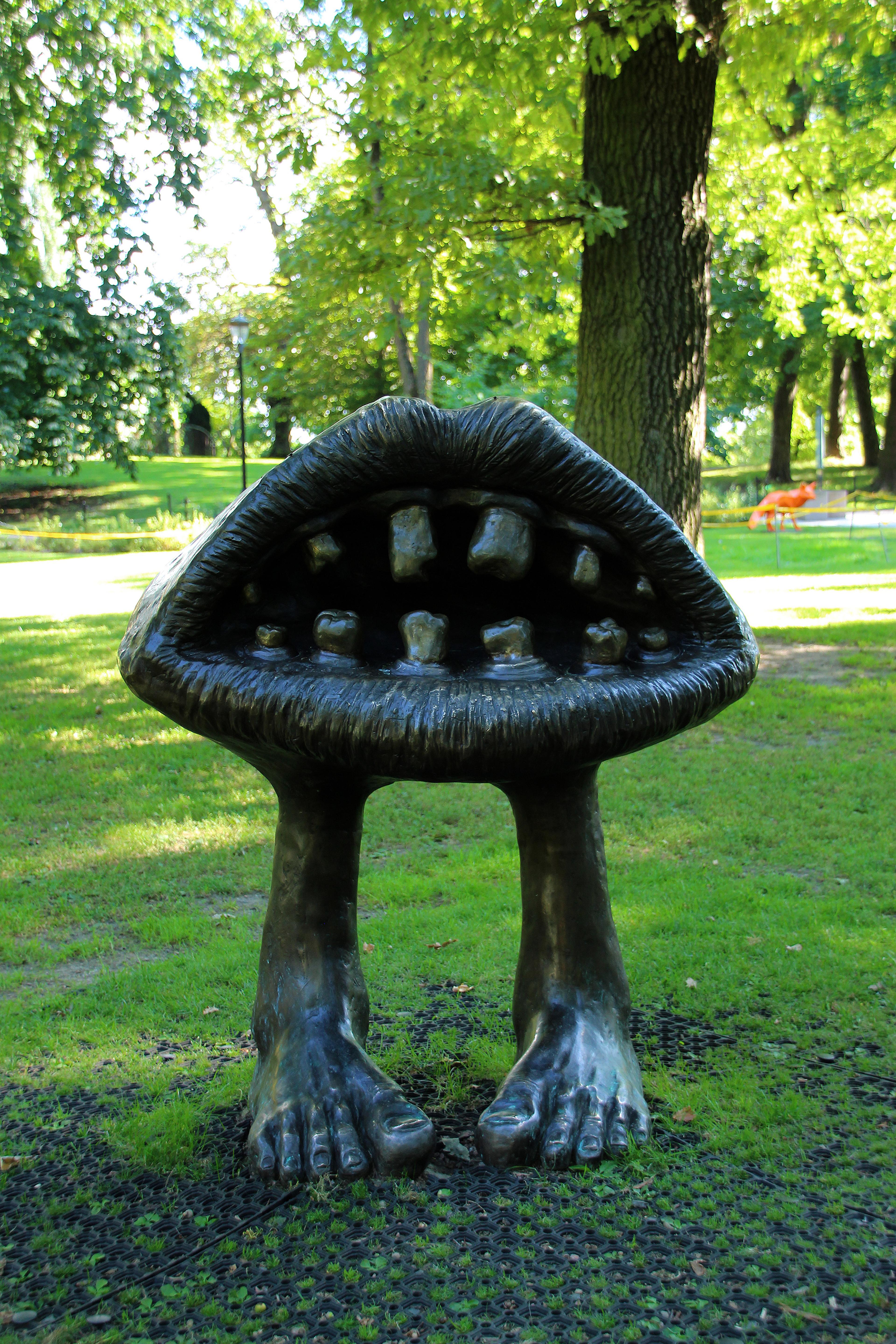 En stor munn, støpt i mørkt metall, står åpen med lepper og tenner står på egne ben i gresset.