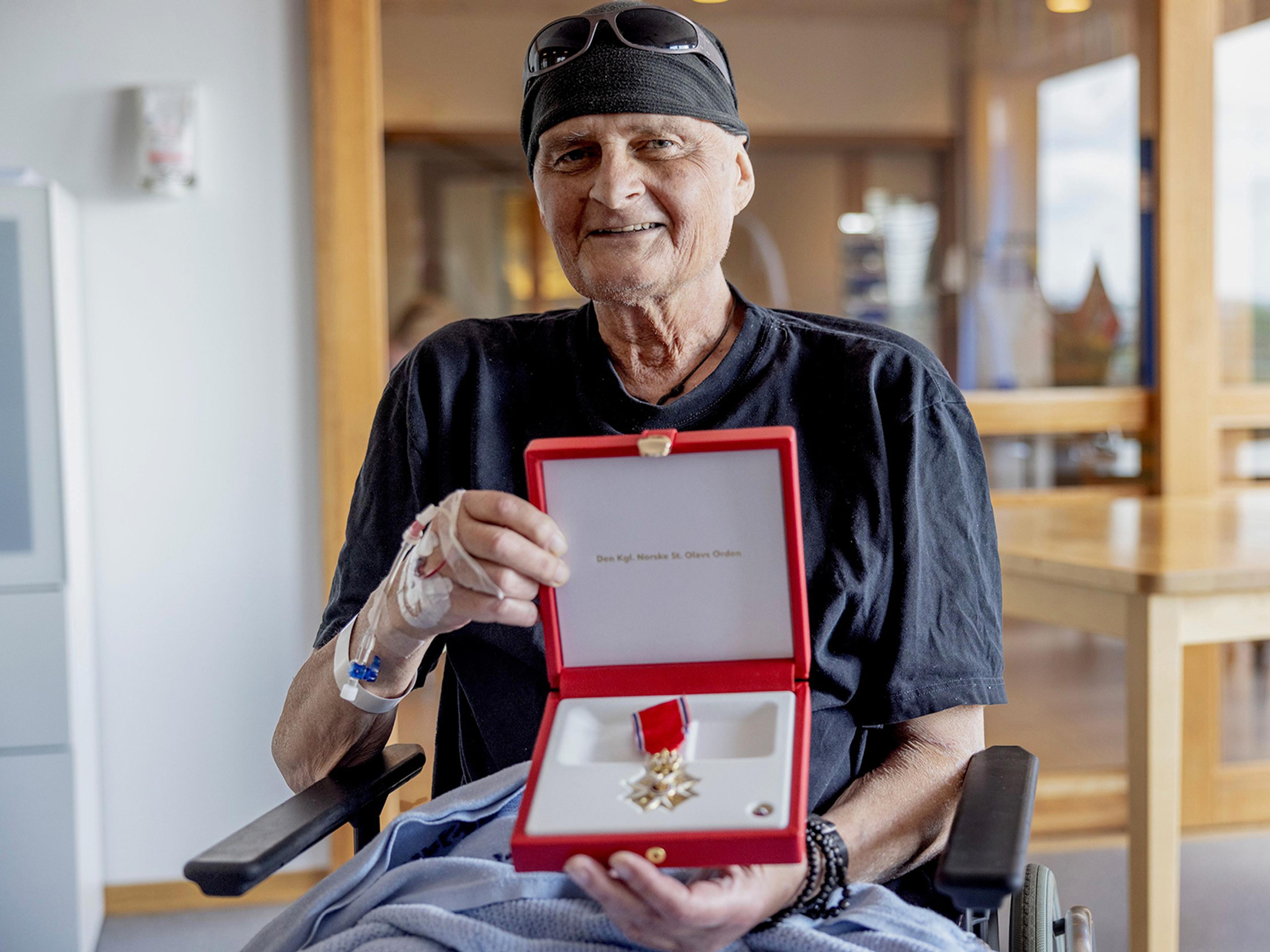En smilende Henden sitter i på sykehuset og viser fram skrinet med St. Olavs Orden.