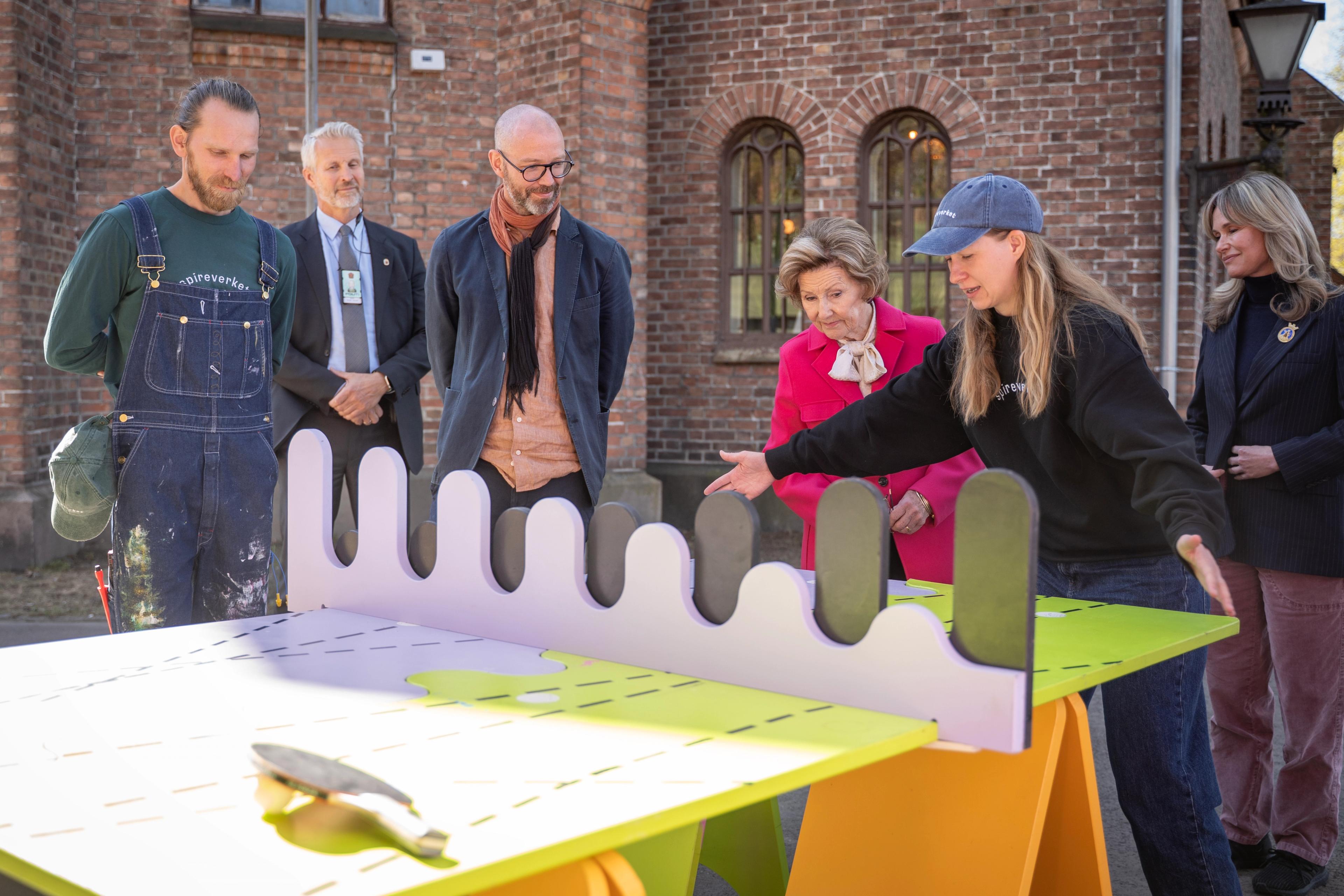 Karoline Olimb holder ved bordendene. Bak står dronningen og ordføreren.