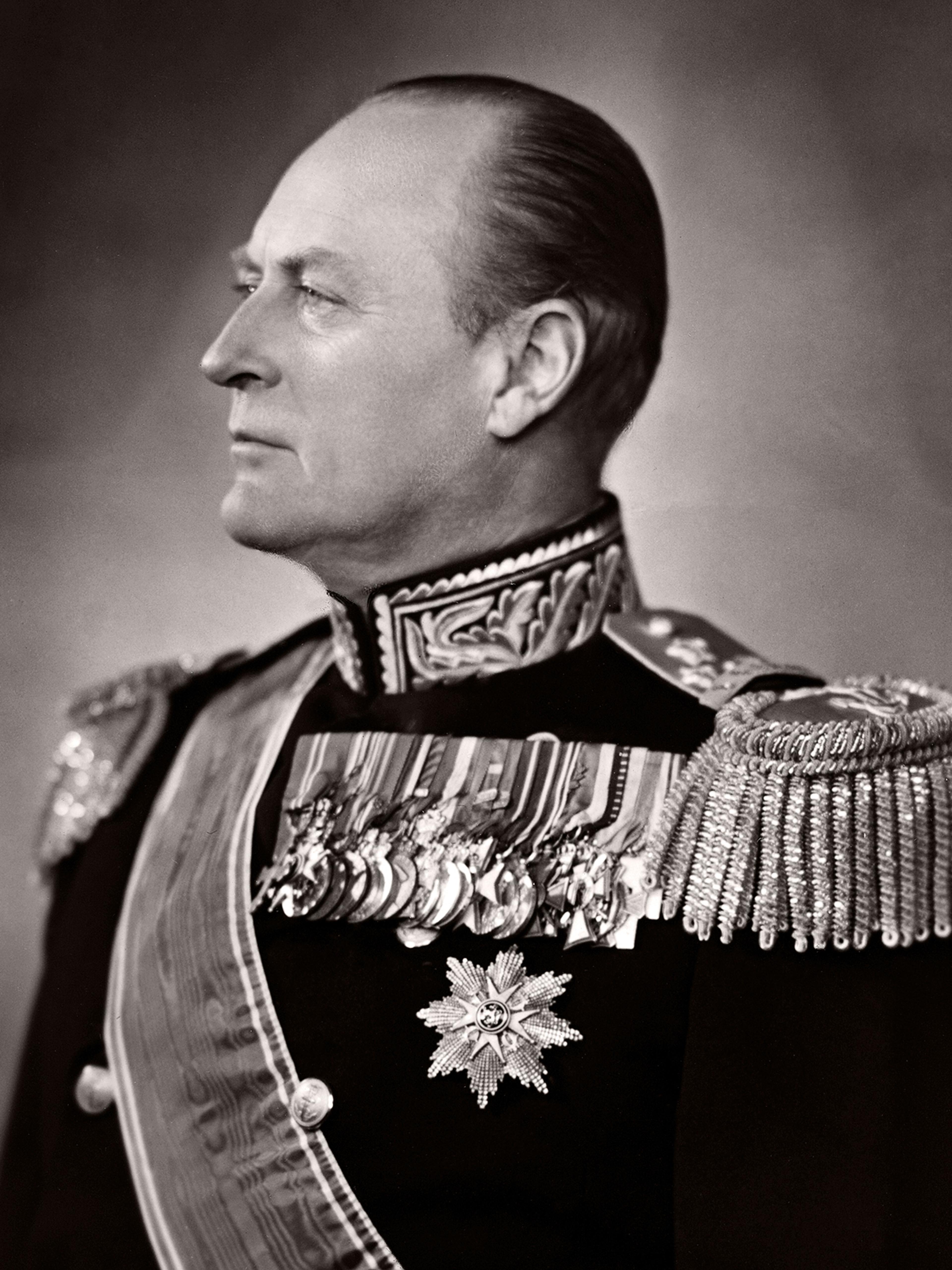 Portrett av Kong Olav i gallauniform med en lang rekke dekorasjoner festet på uniformsjakken.