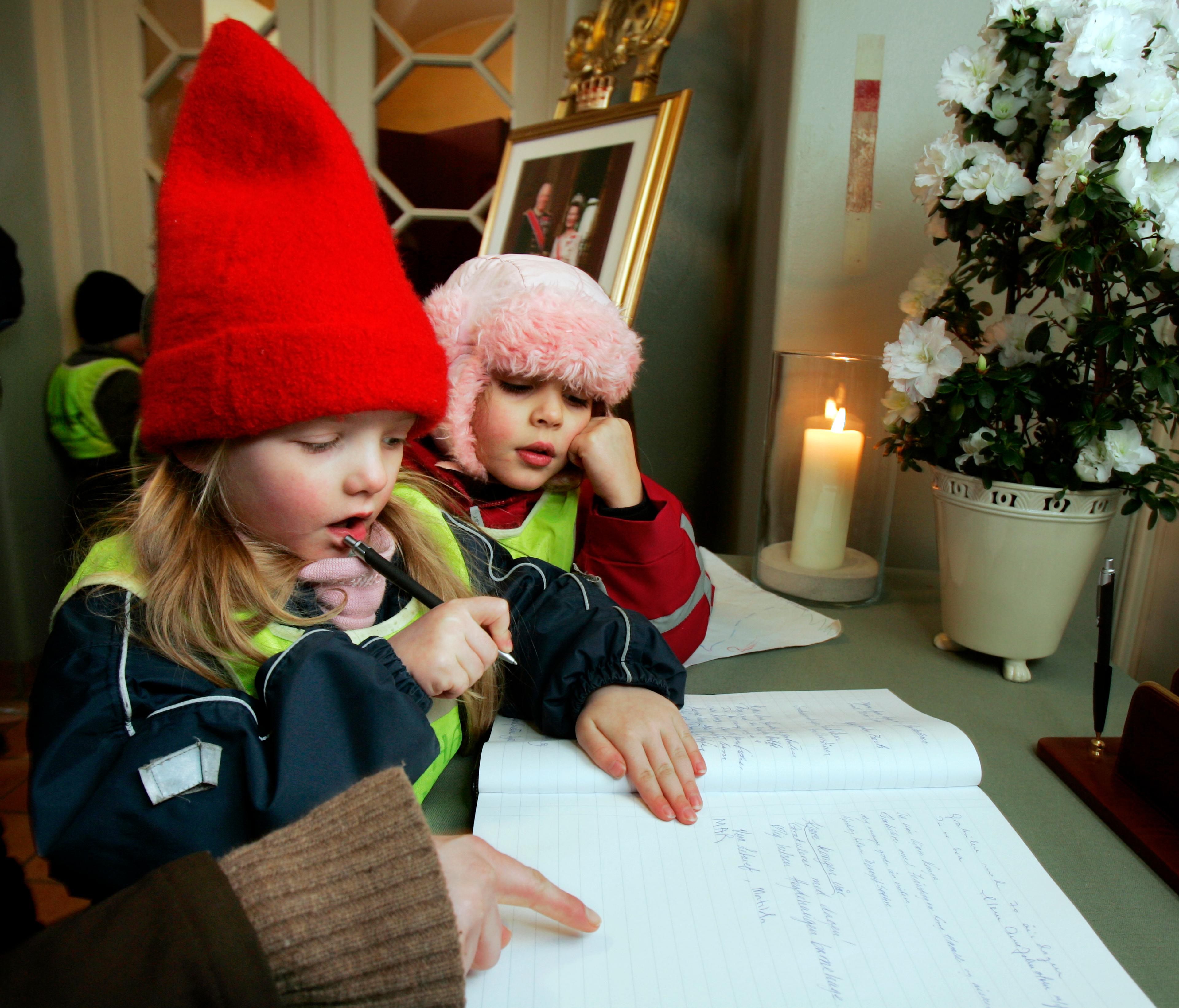 To små barn med parkdresser og luer. Den ene har en penn i hånden og skal til å skrive.