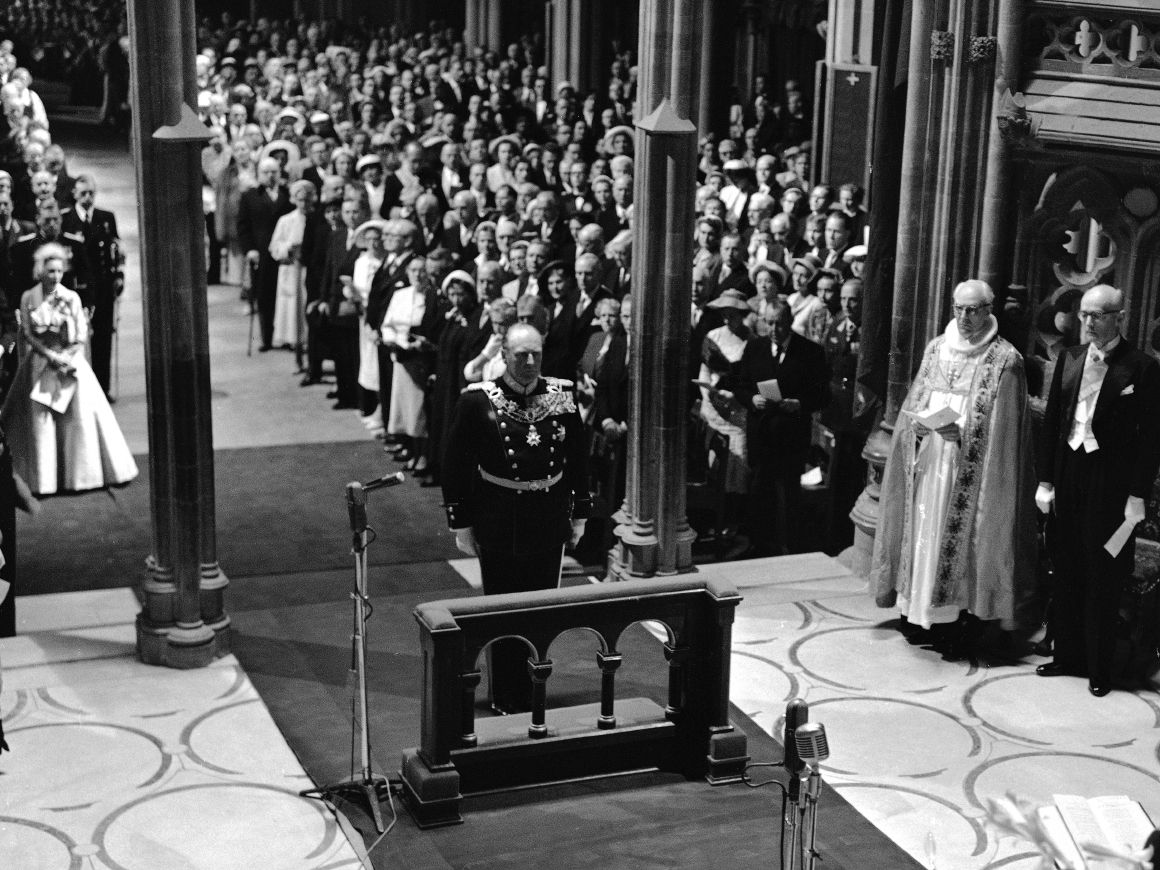 Sort-hvittbilde fra Nidarosdomen. Kong Olav står i gallauniform fremst i kirken og vil snart knele for å motta velsignelsen.