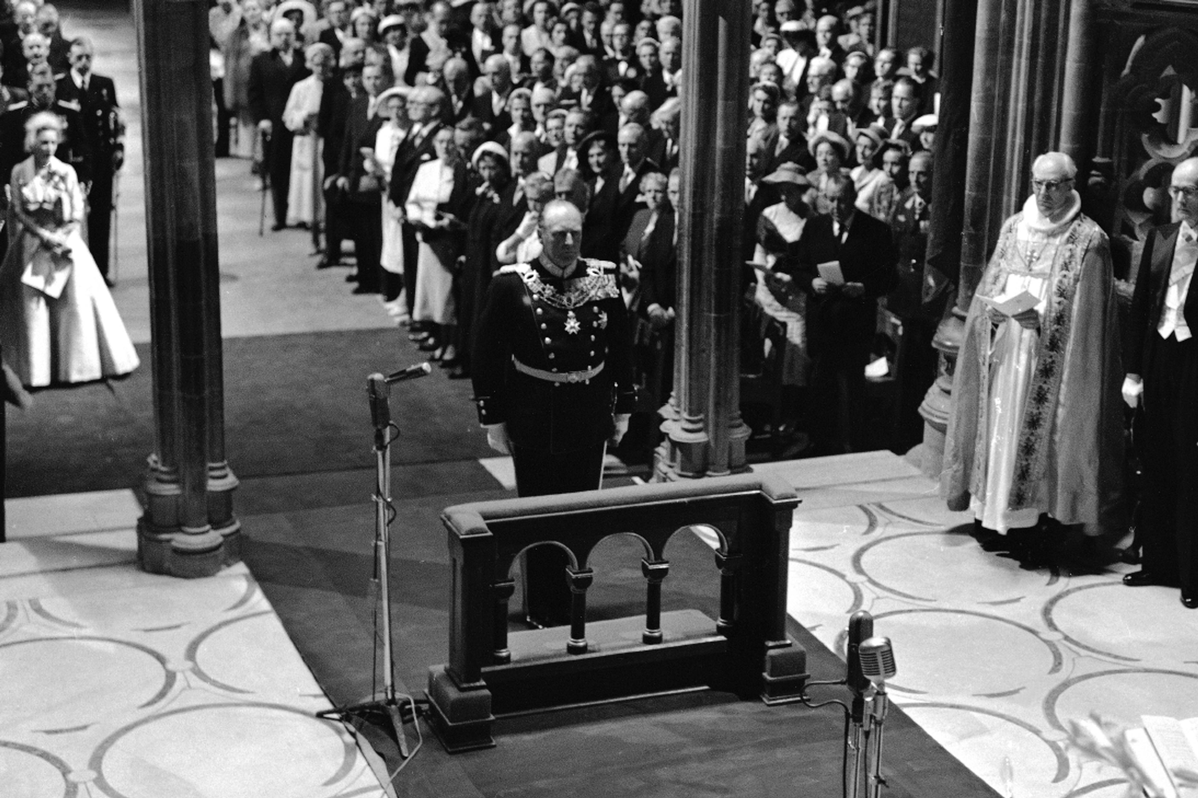 Sort-hvittbilde fra Nidarosdomen. Kong Olav står i gallauniform fremst i kirken og vil snart knele for å motta velsignelsen.