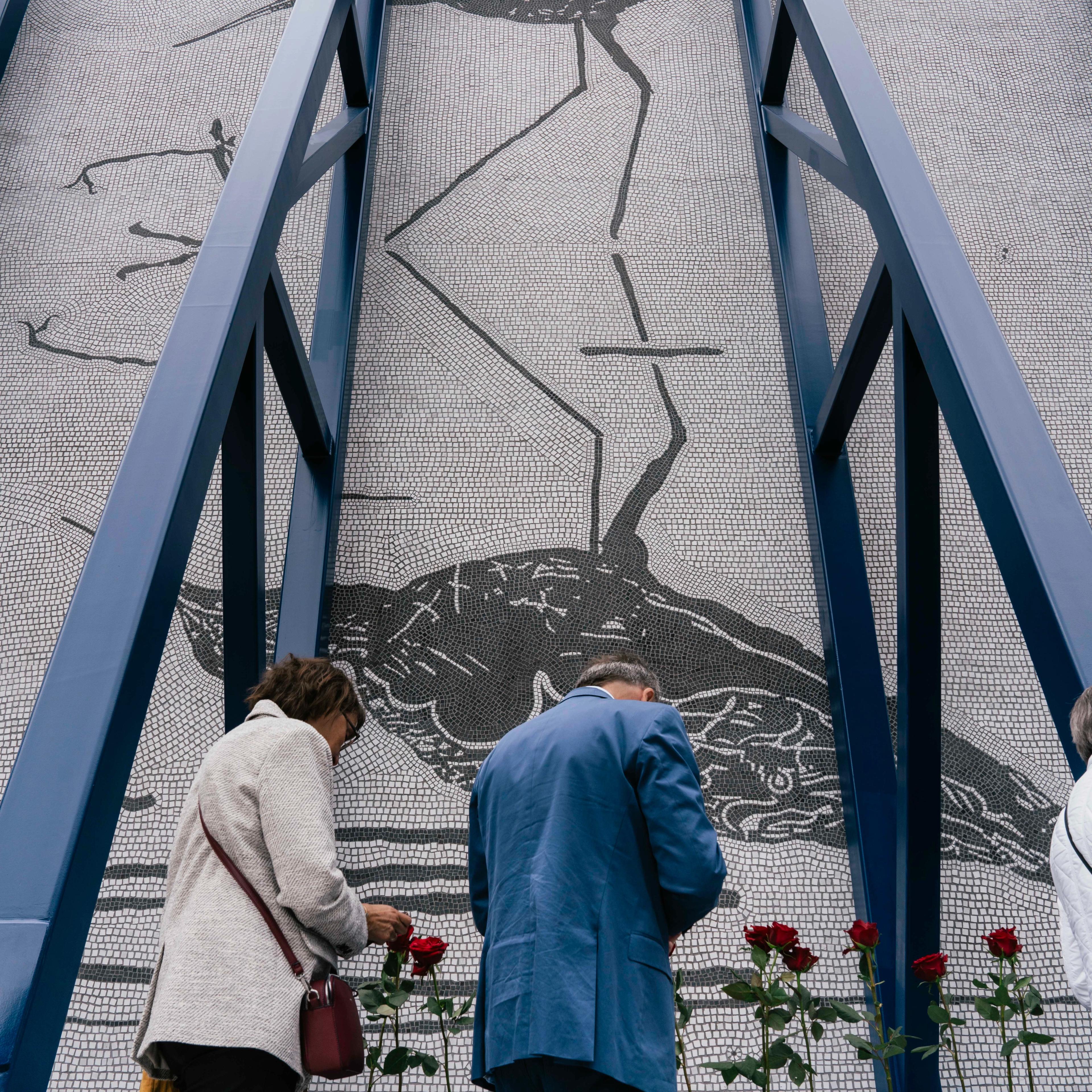 To besøkende - kanskje pårørende - står ved rosene satt i bærebjelken på monumentet.
