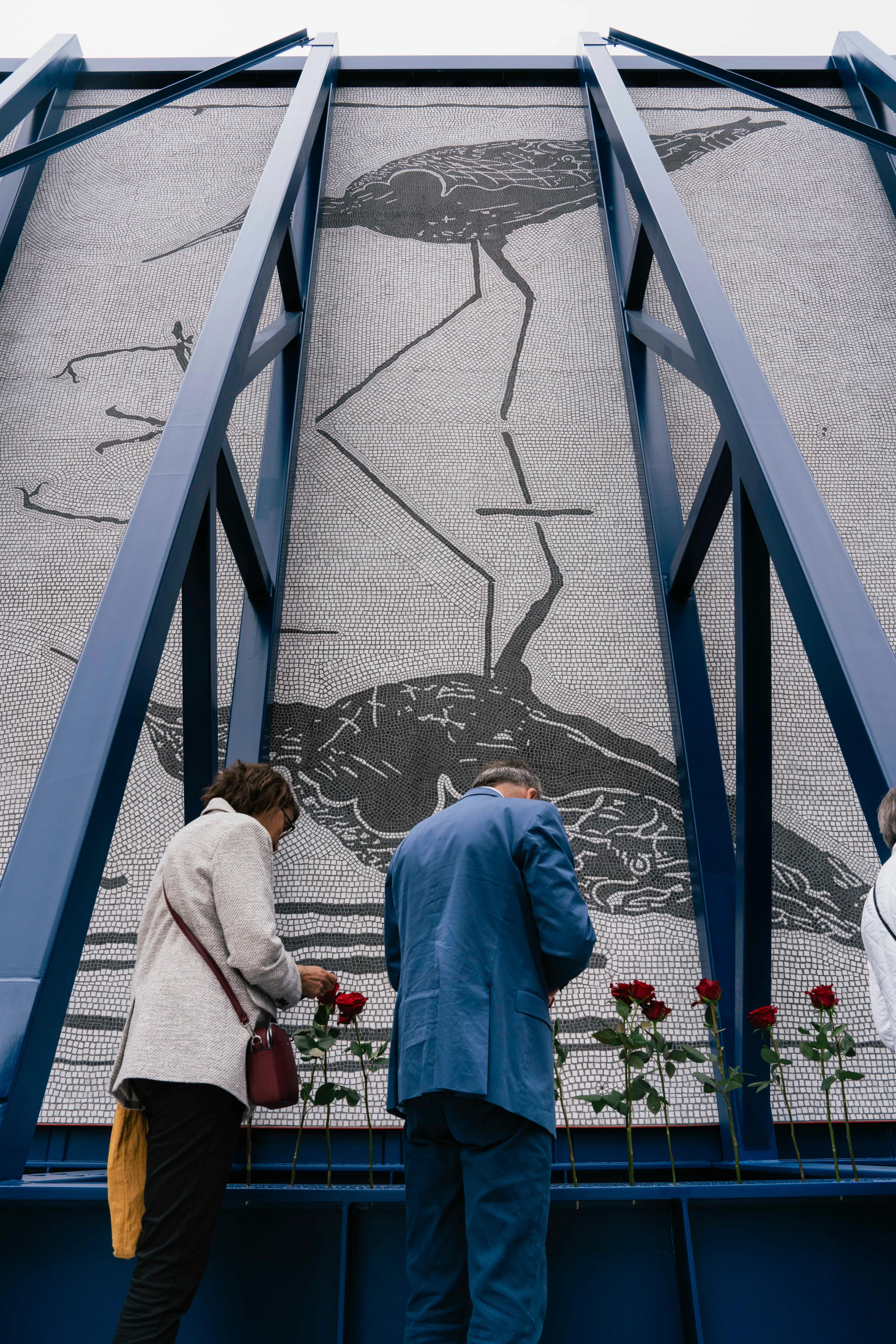 To besøkende - kanskje pårørende - står ved rosene satt i bærebjelken på monumentet.
