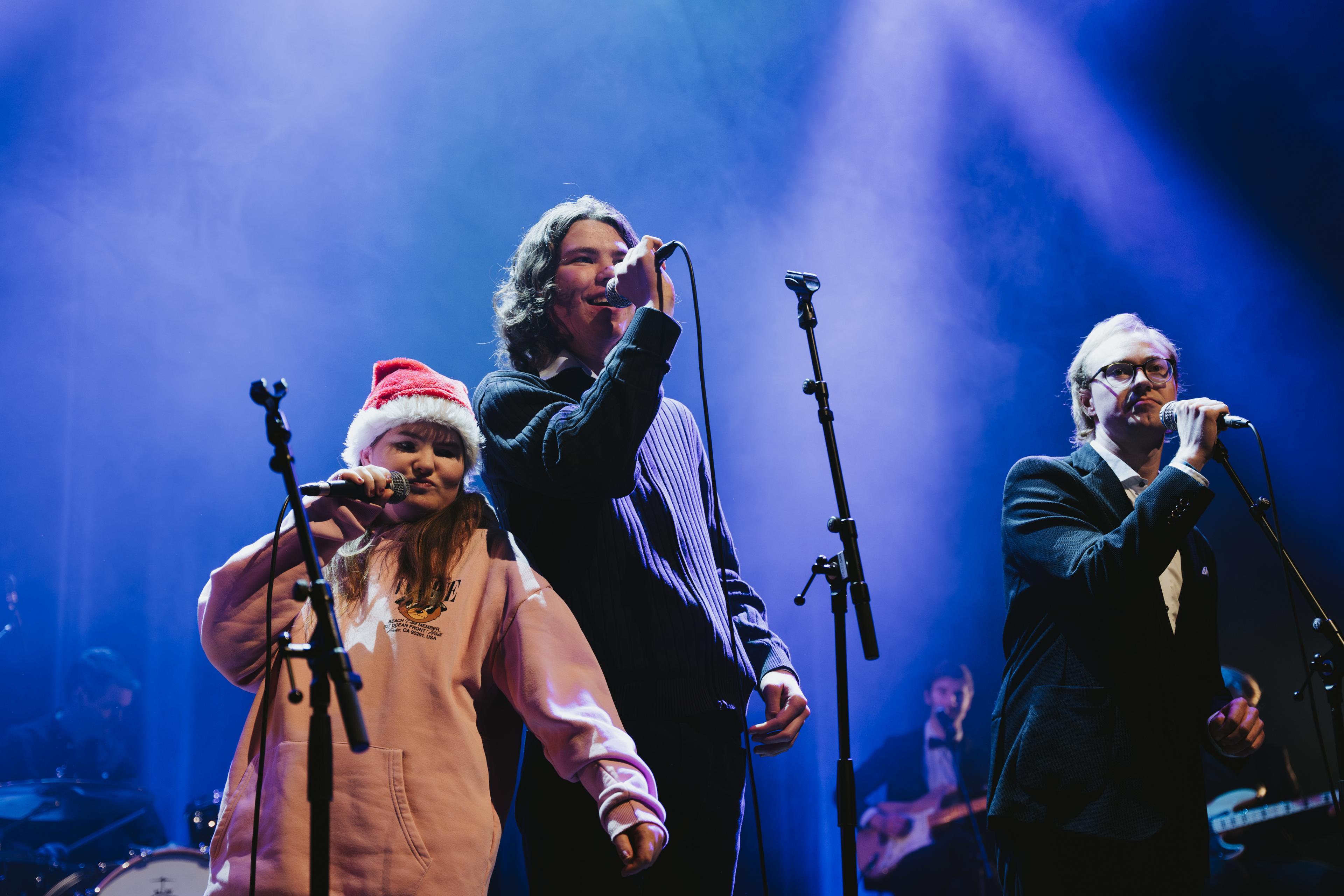 Tre songarar på scena, to menn og ei kvinne med nisselue.