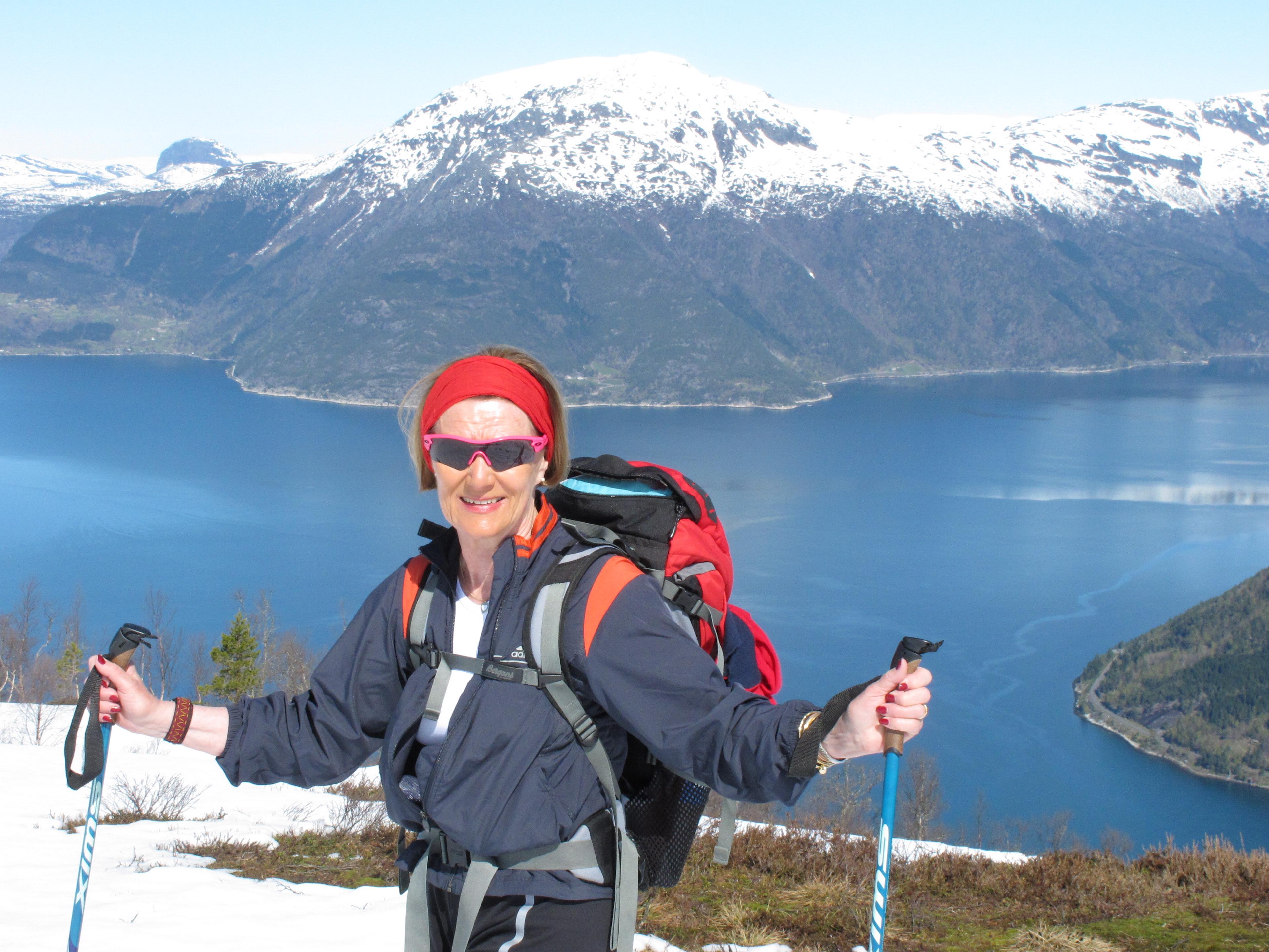 Dronning Sonja i turutstyr, solbriller og skistaver. Bak henne ligger en flott utsikt med snødekte fjell og en innsjø.
