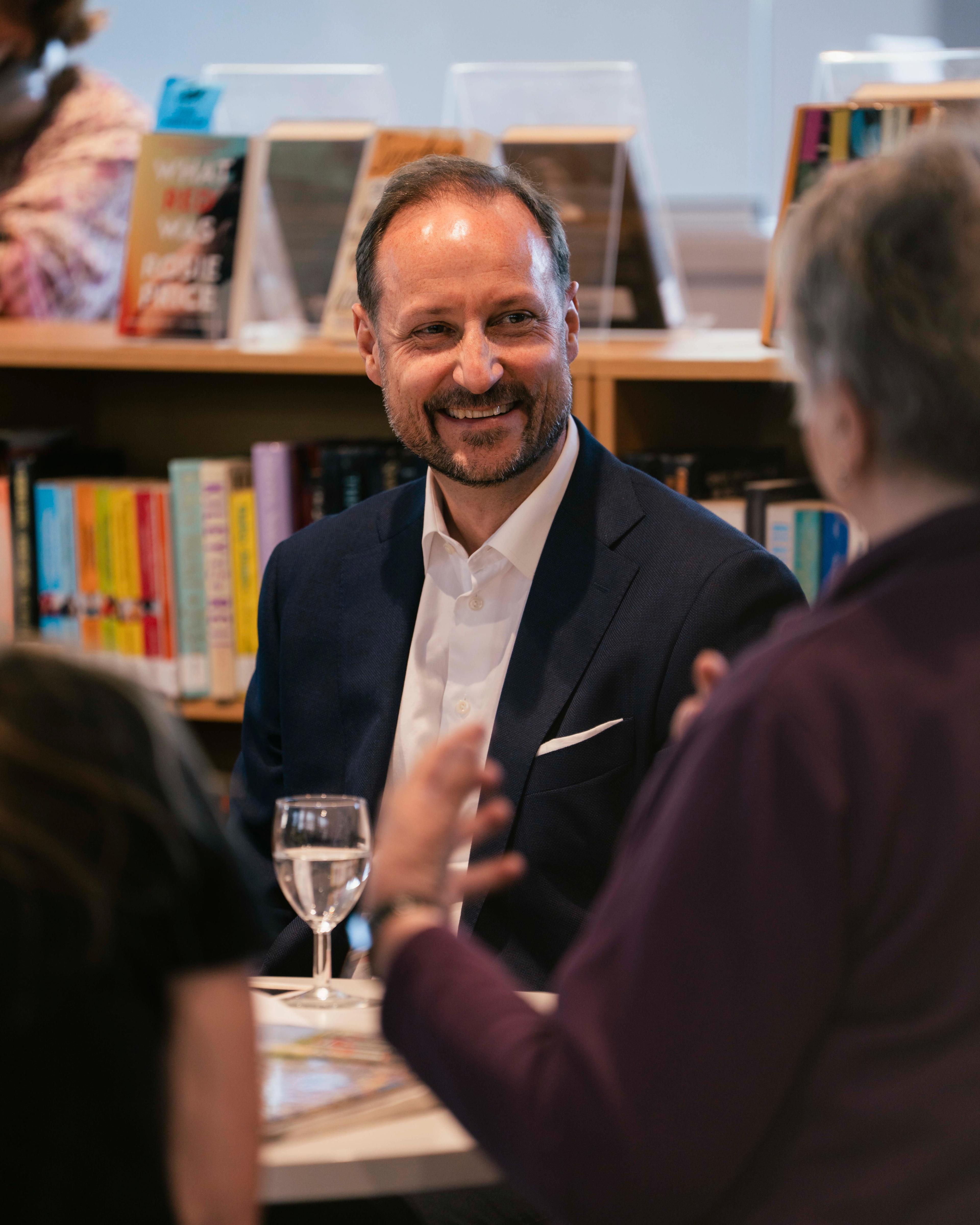Kronprins Haakon smiler til en kvinne som han er i en samtale med rundt bordet på biblioteket