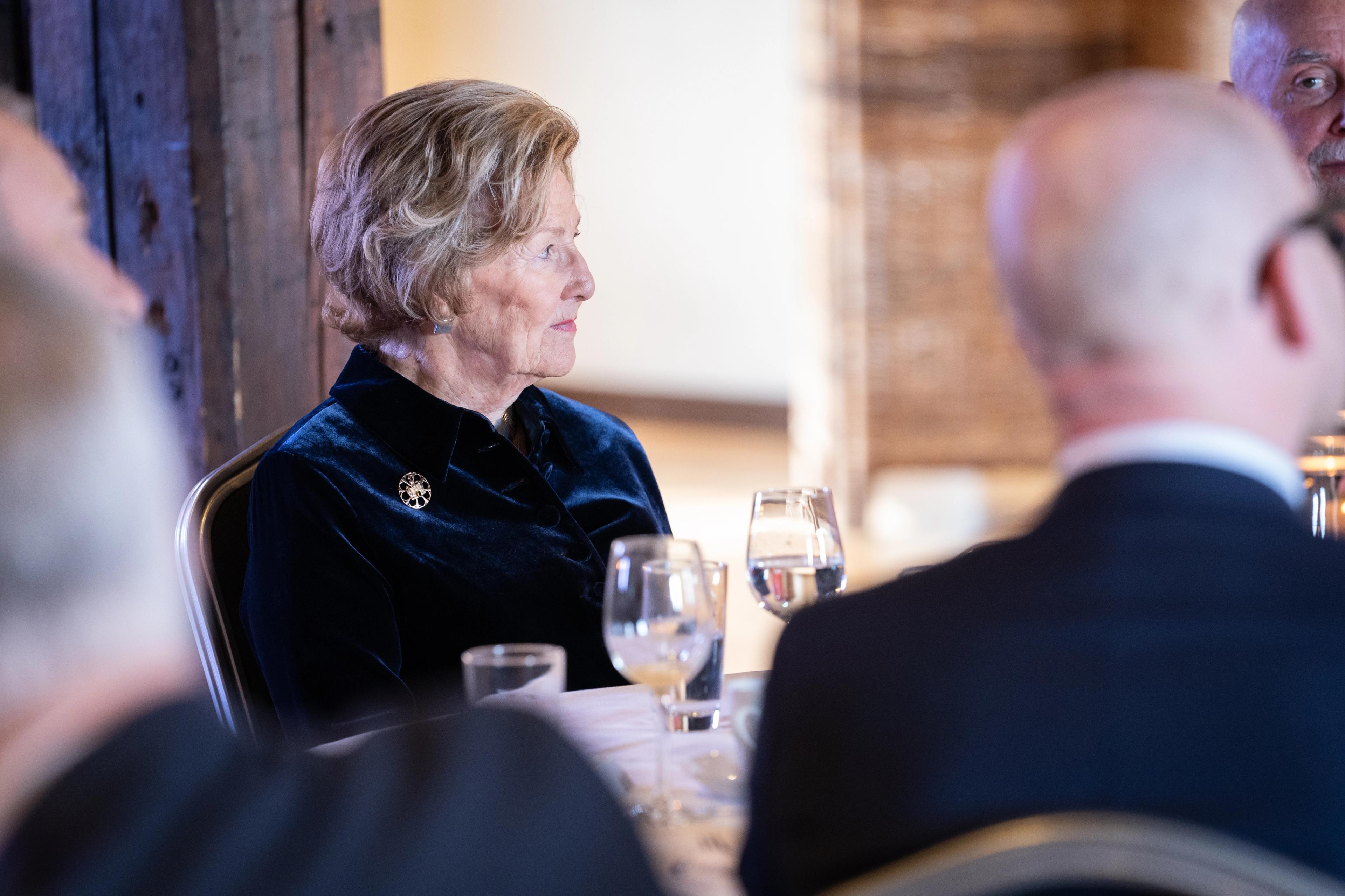 Dronningen ikledd blå jakke sitter rundt et bord og lytter til foredragsholderne.