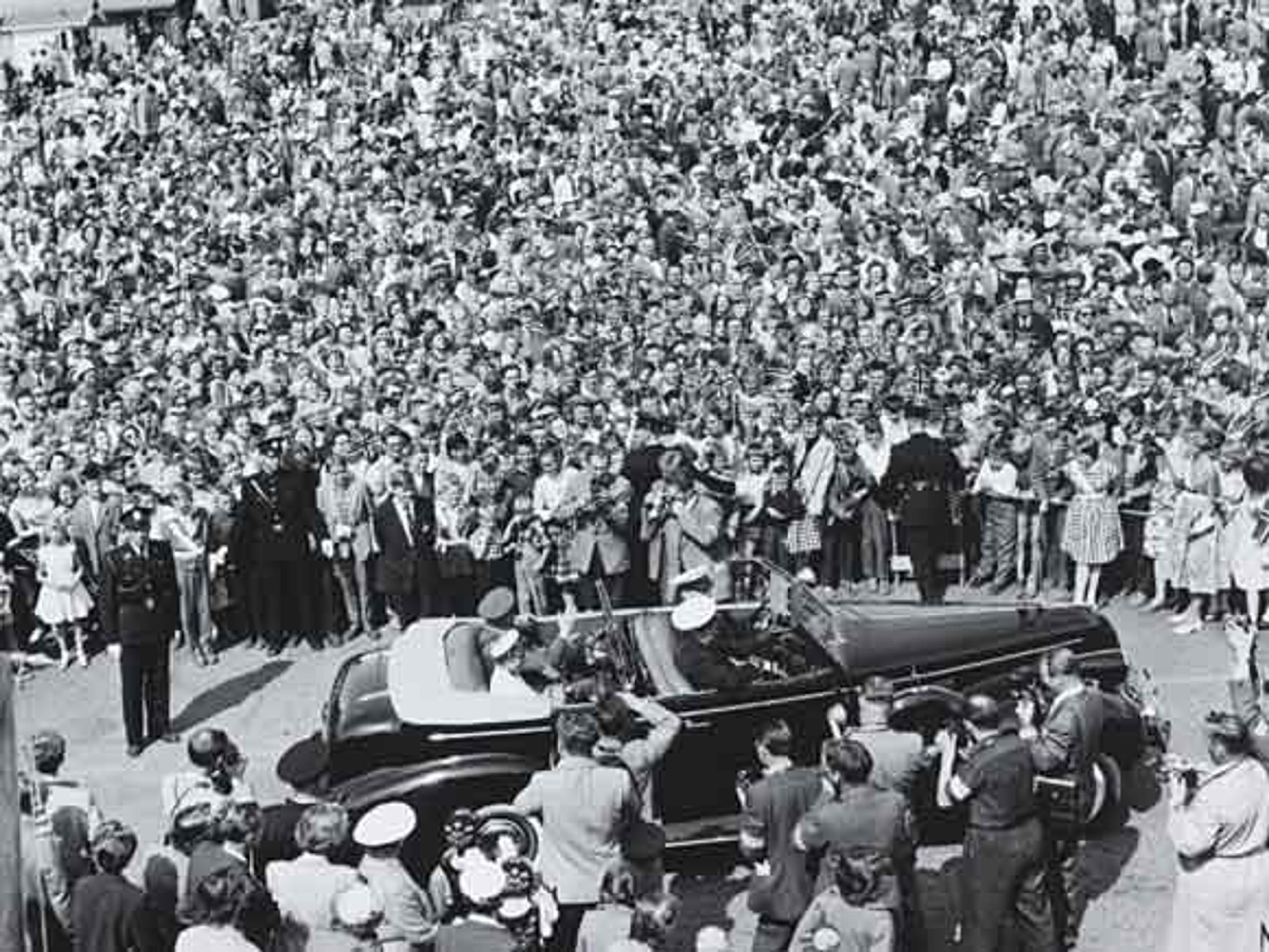 Bilen med Kong Olav sett ovenfra/fra siden, omkranset av en stor menneskemengde.